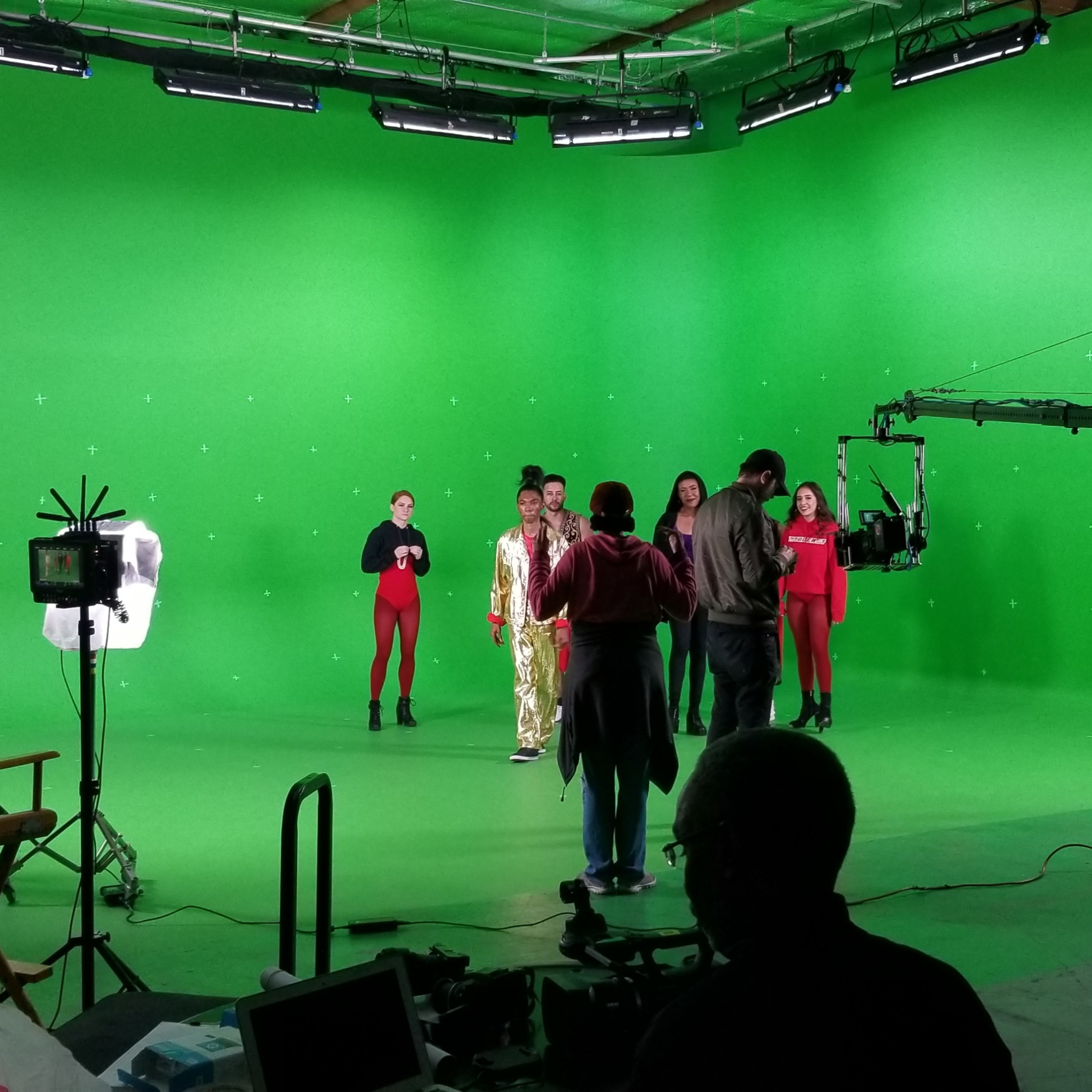 A group of people performs on a green screen soundstage with several lights positioned around the set.