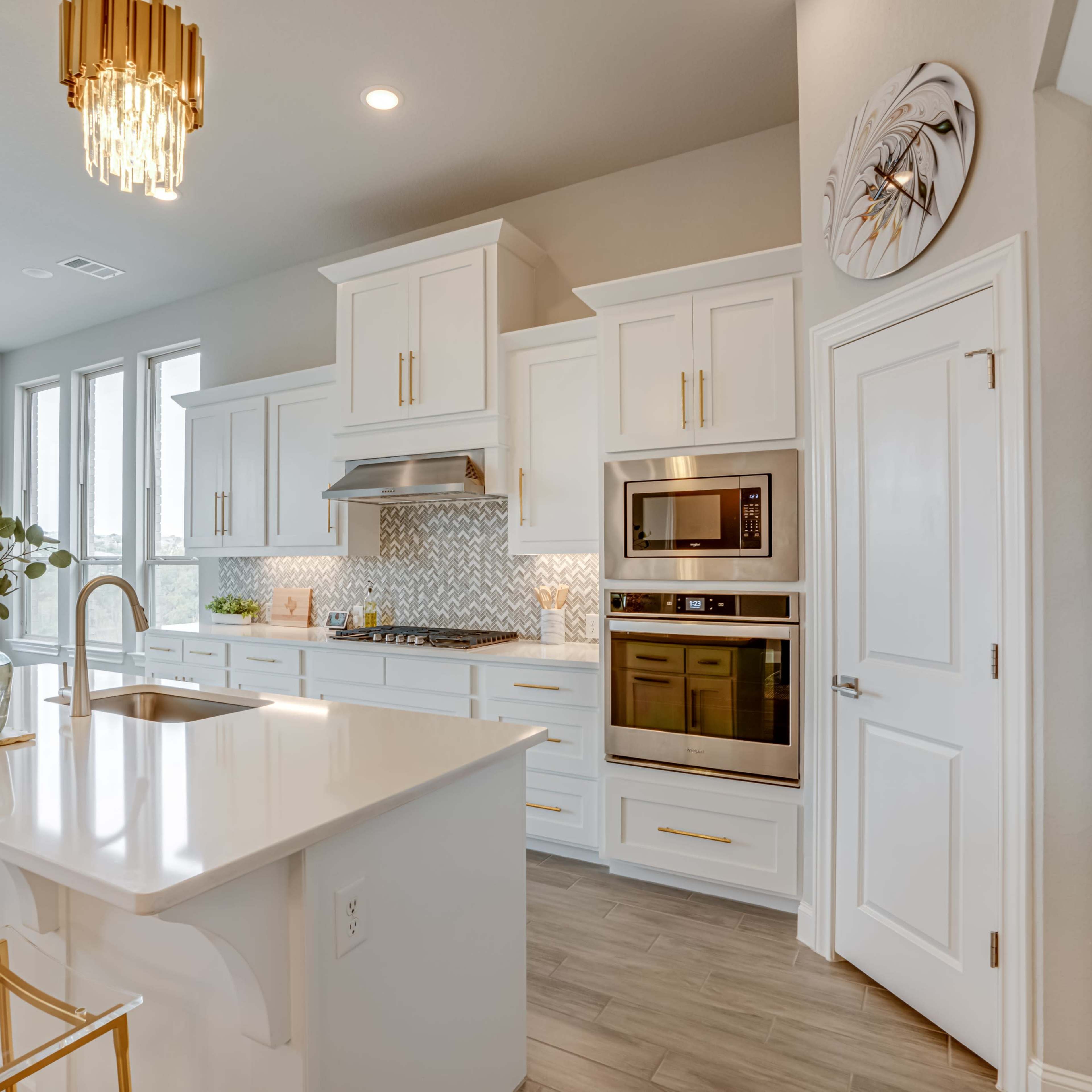 A modern kitchen with white cabinetry, stainless steel appliances, a large island with a sink, and gold accents in the light fixtures and bar stools.