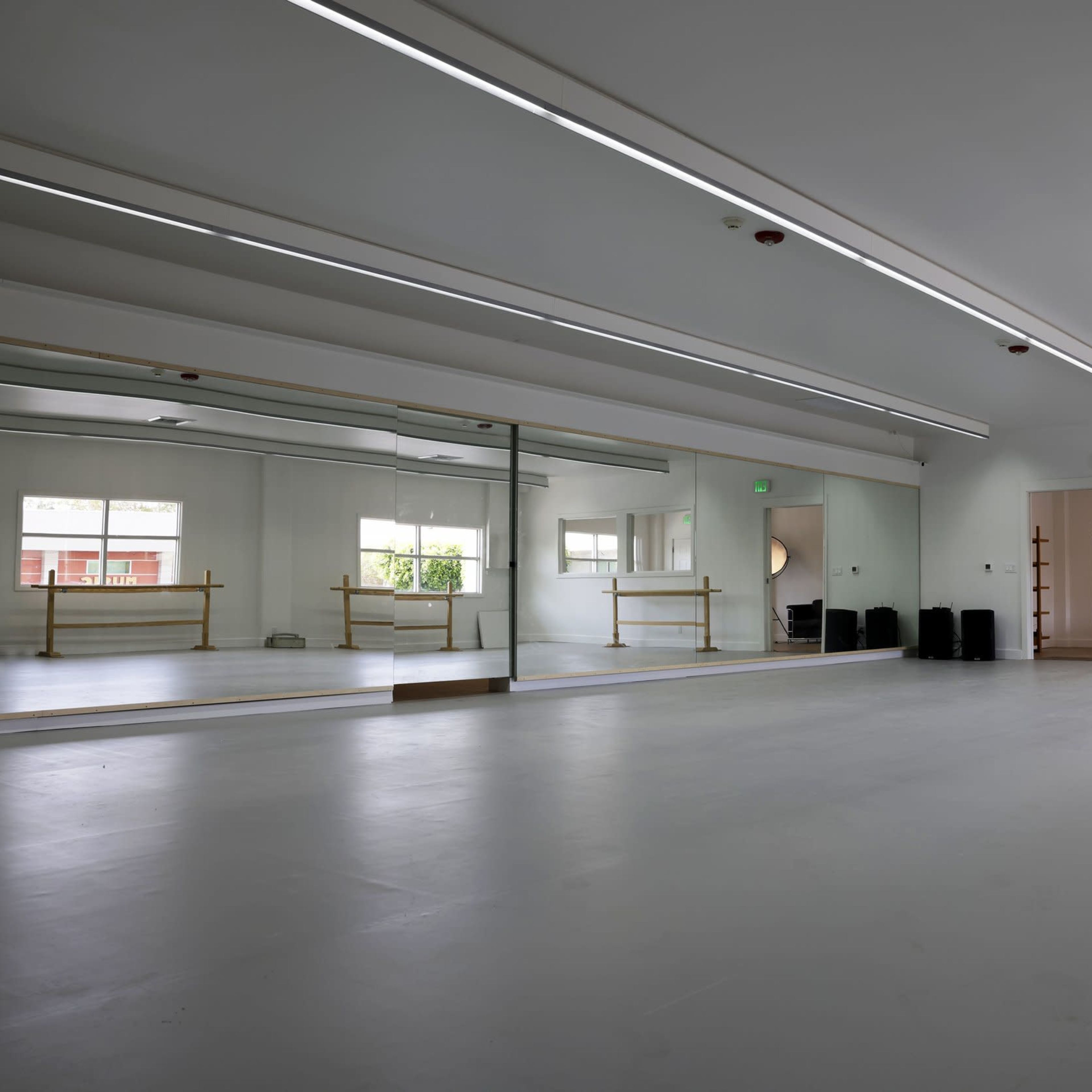 A spacious dance studio with mirrored walls, overhead lighting, and a ballet barre along one side.