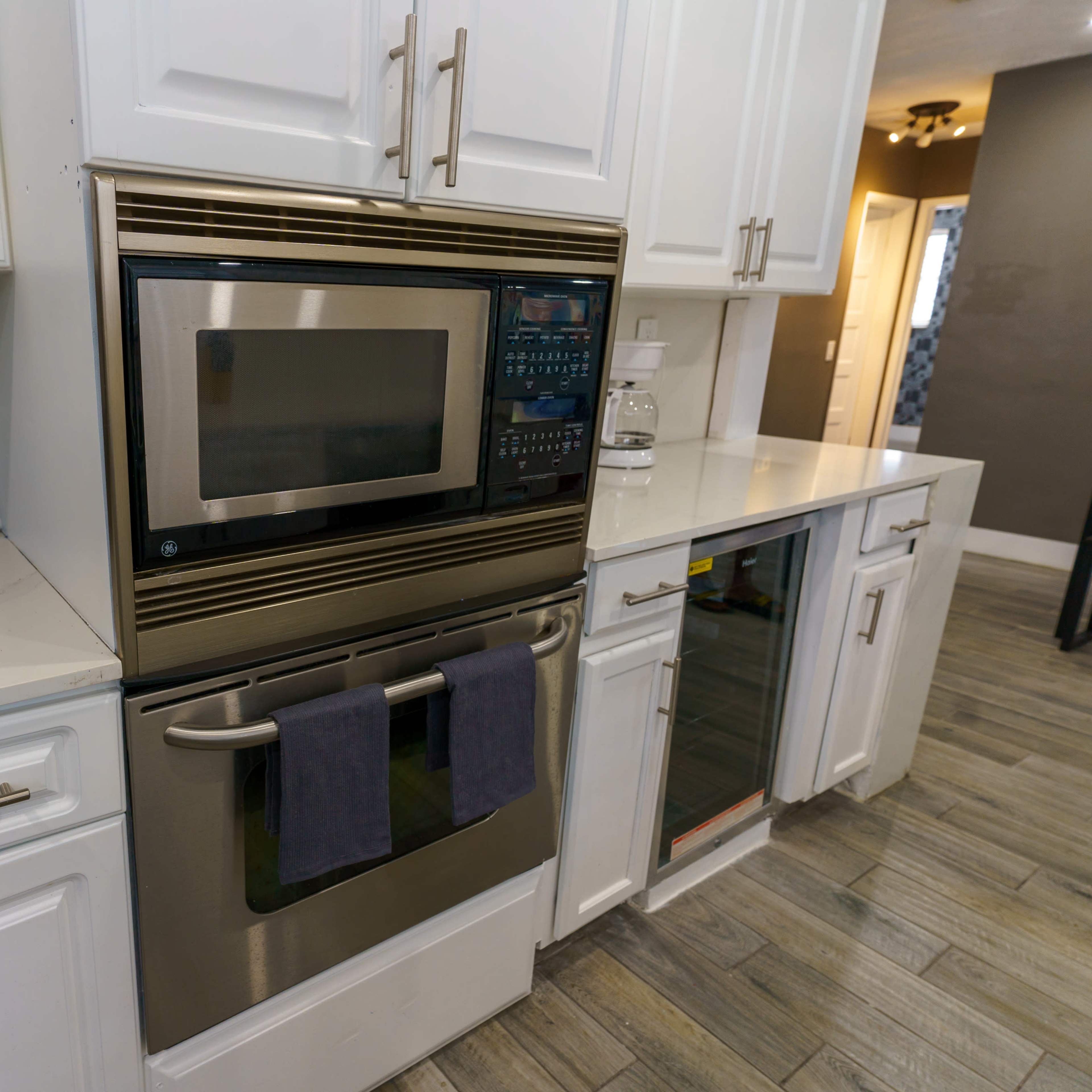 A modern kitchen countertop with a stainless steel microwave and oven combination, alongside a small microwave and a countertop wine cooler.