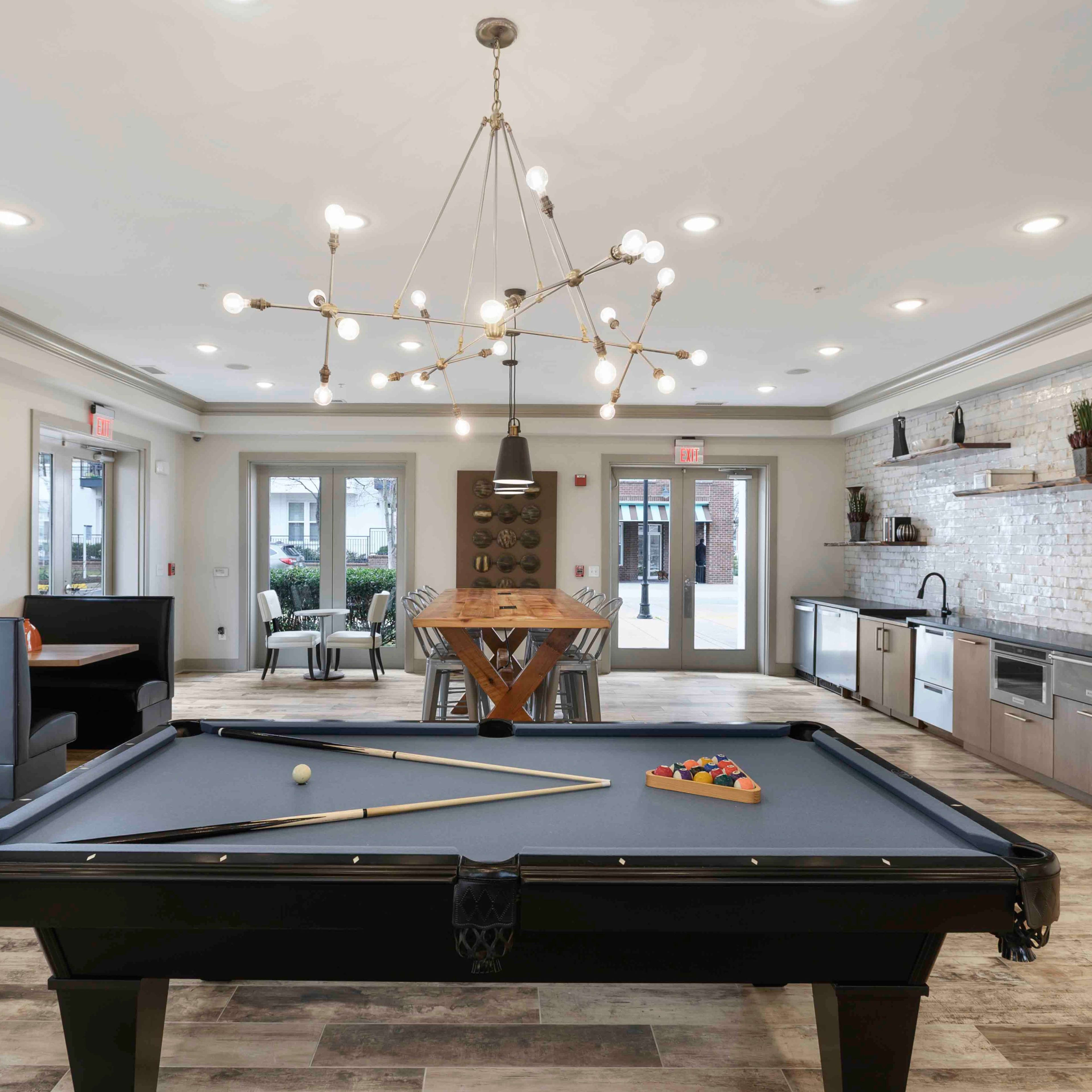 A modern recreation room featuring a pool table, dining table, and kitchen area with a decorative wall.
