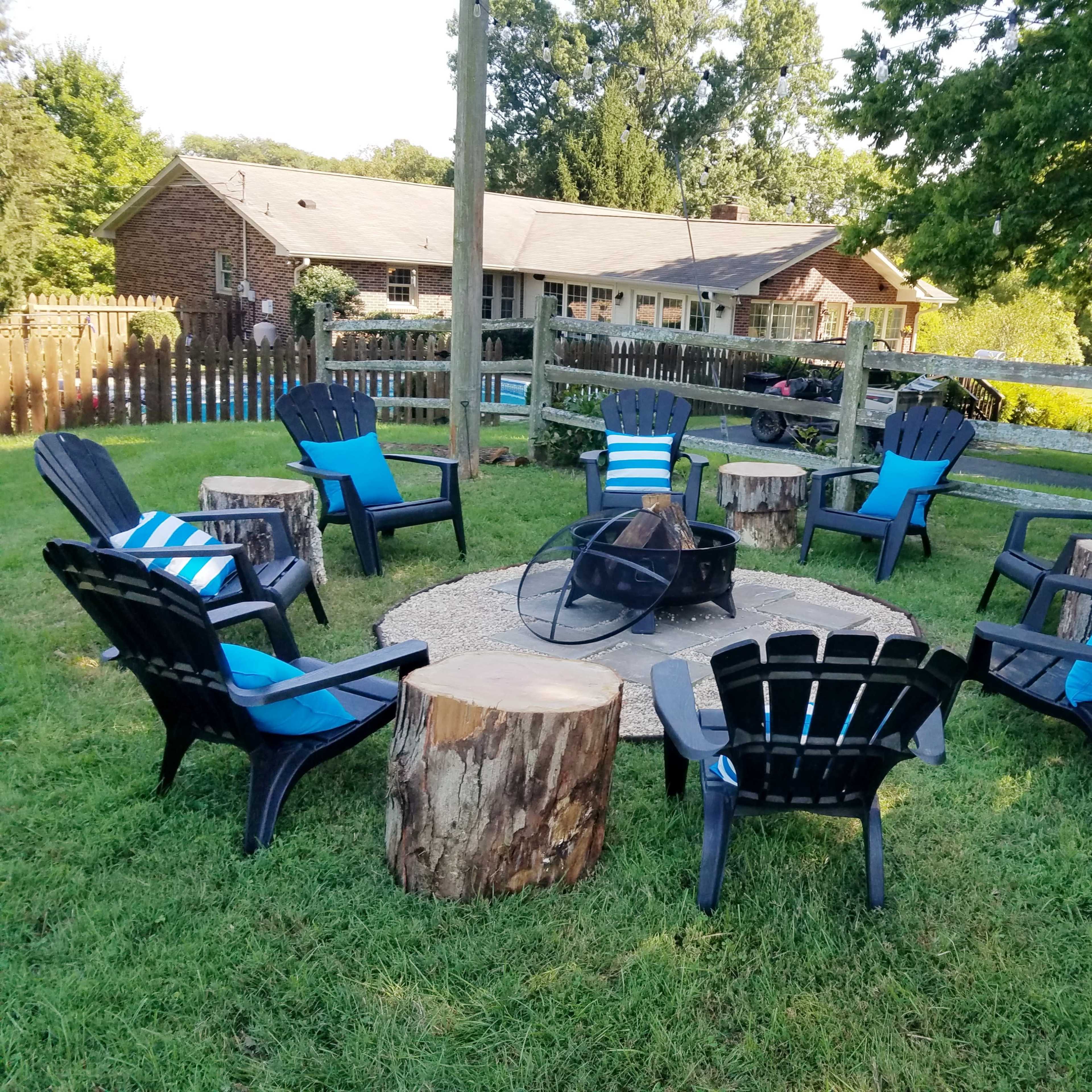 A circular seating area made of black chairs around a fire pit, surrounded by grassy terrain and rustic wooden elements.