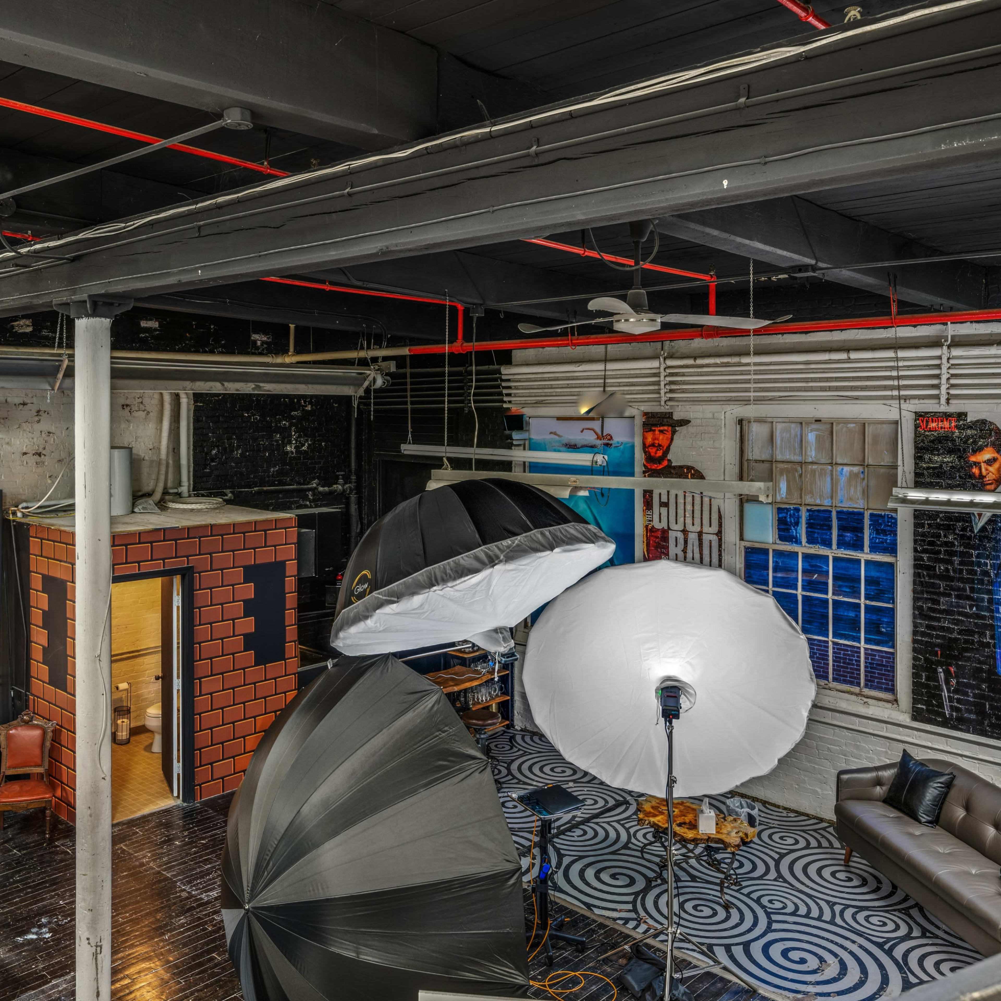 A spacious studio with various photography equipment, including large softbox lights, a red-brick backdrop, and different seating areas.
