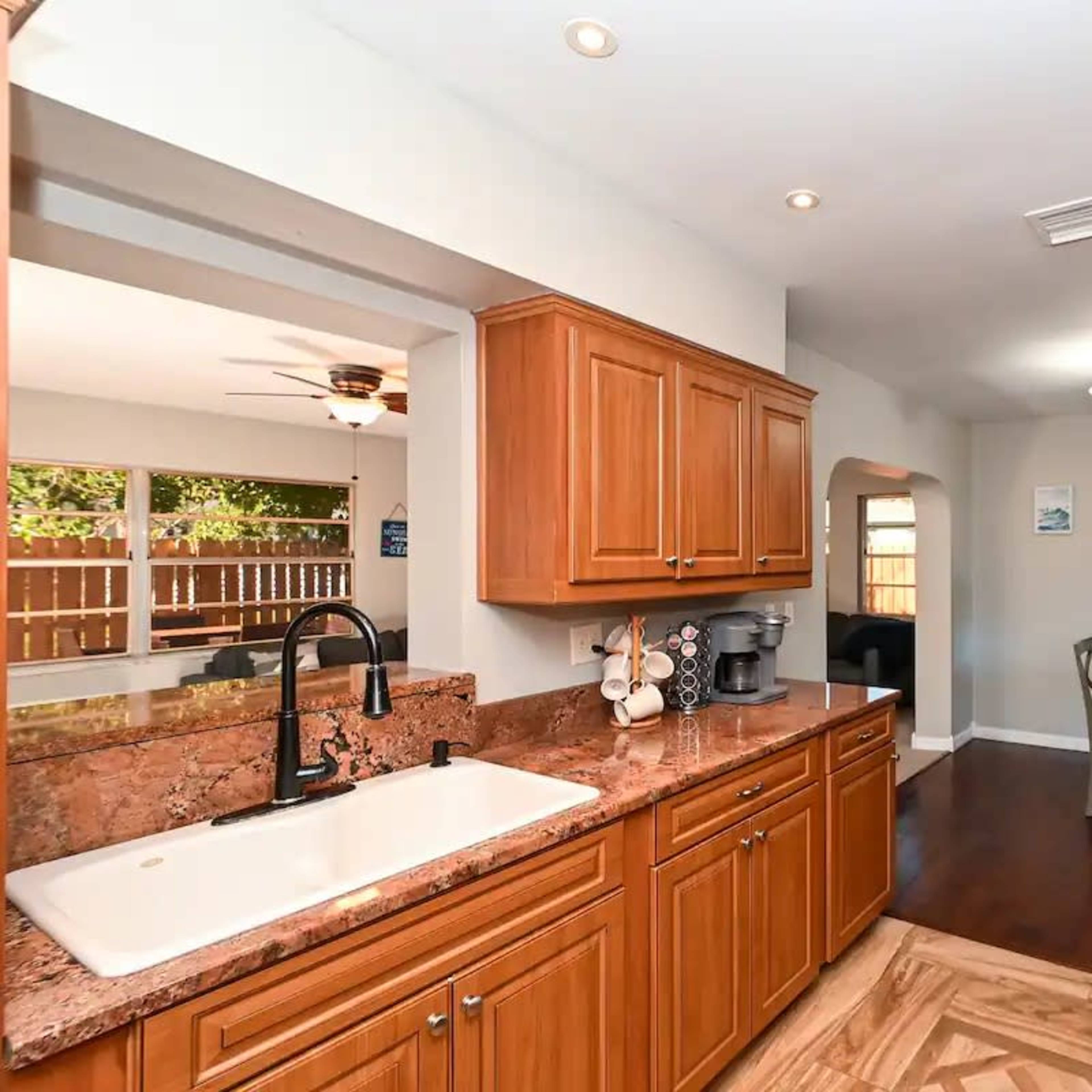 A modern kitchen with wooden cabinets, a stone countertop, and an open layout leading to a dining area.