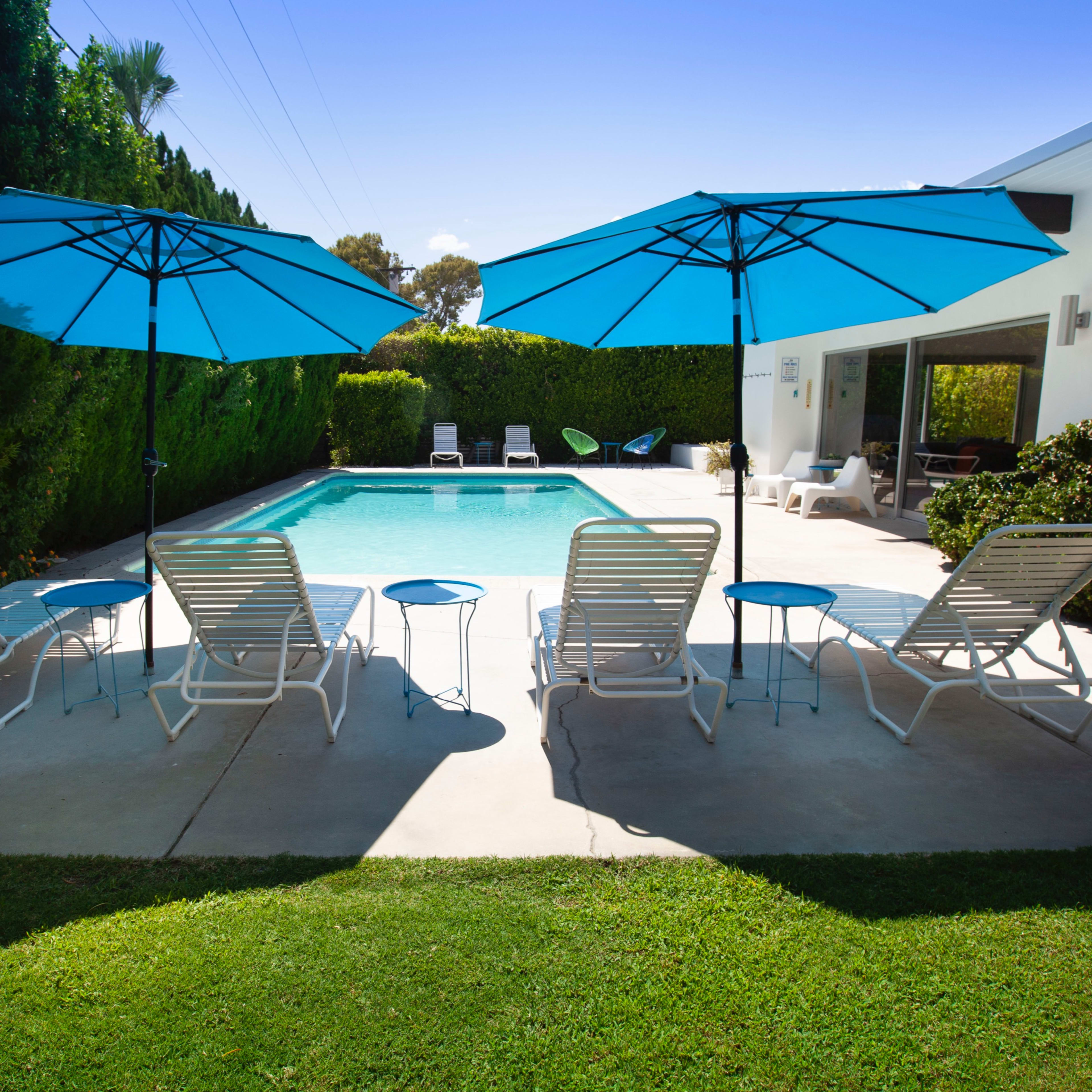 A swimming pool surrounded by lounge chairs and blue umbrellas in a landscaped backyard.