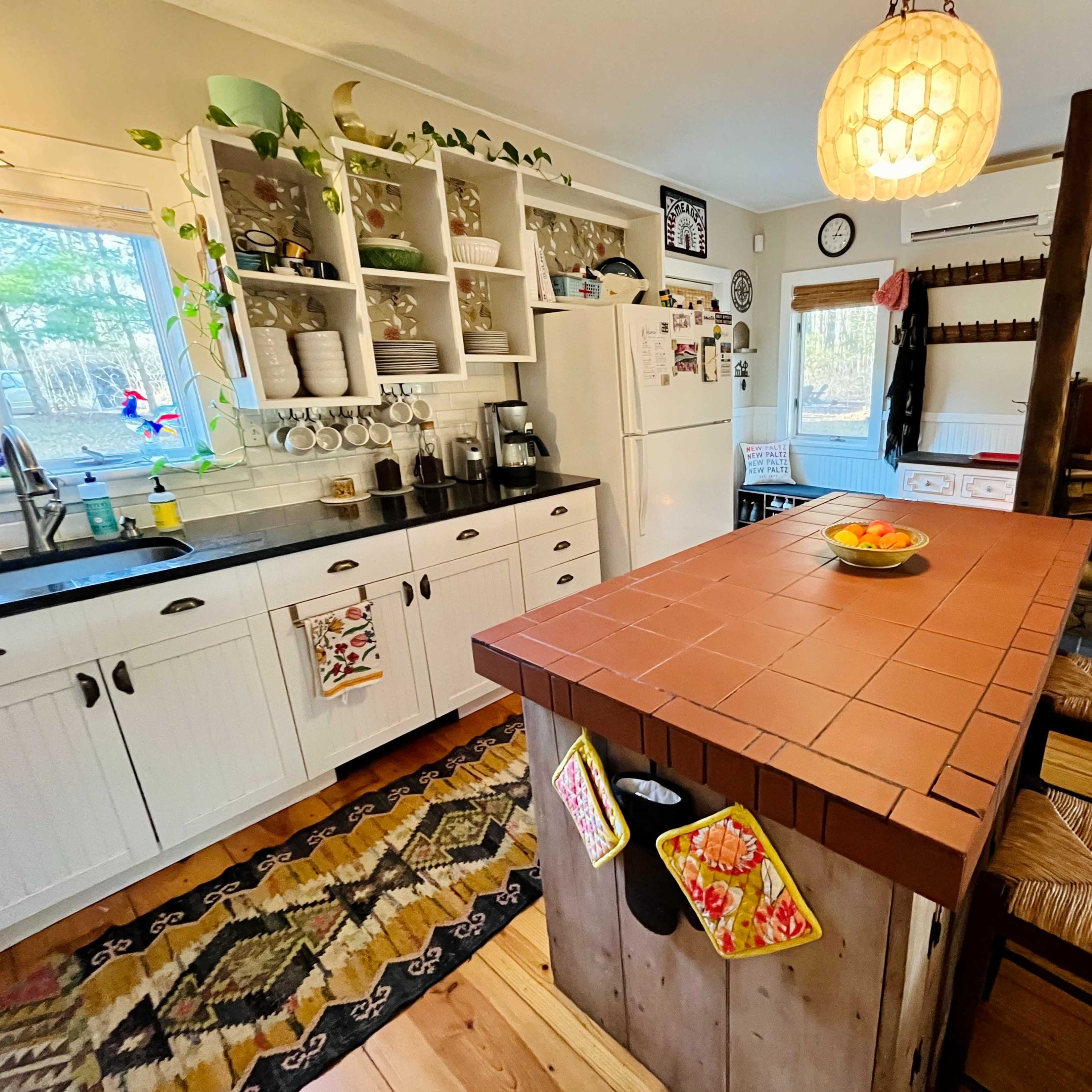 The kitchen features a central island with a tiled top, surrounded by wooden stools, and is equipped with white cabinets and a cozy wood-burning stove in the corner.