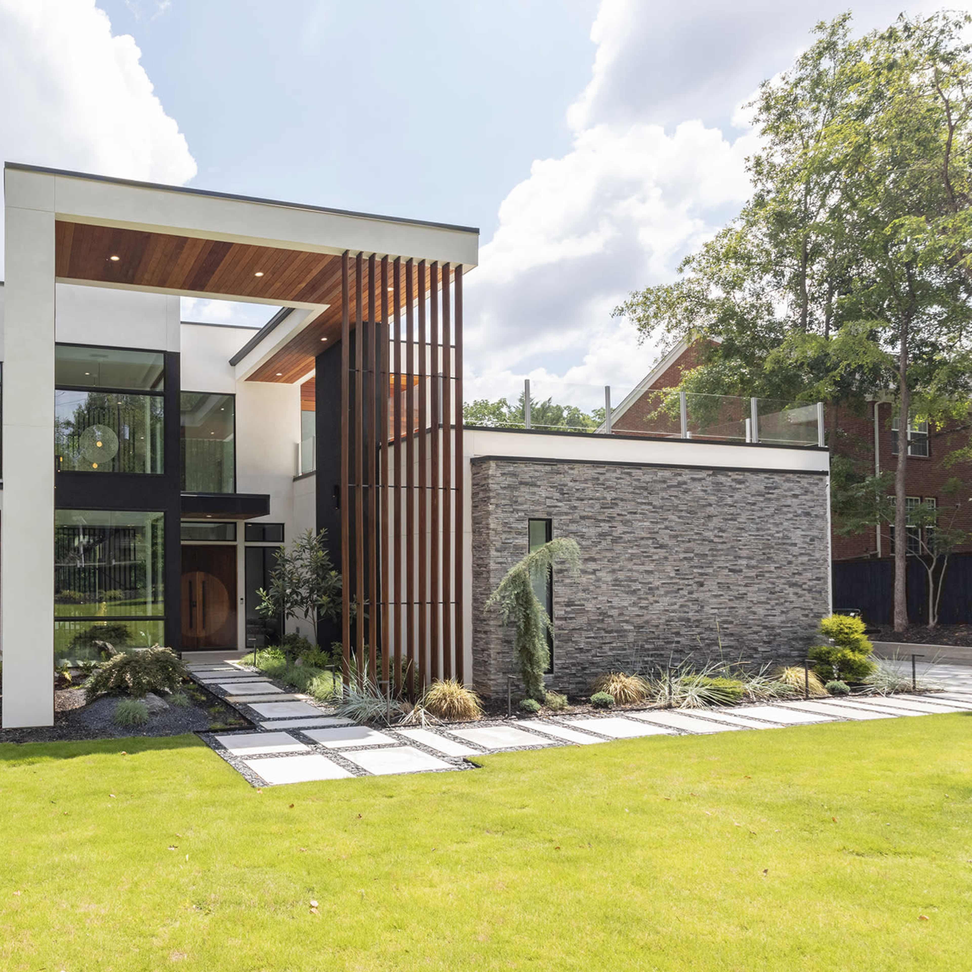 A modern house featuring a combination of wood, stone, and glass elements, with a landscaped front yard and a large entryway.