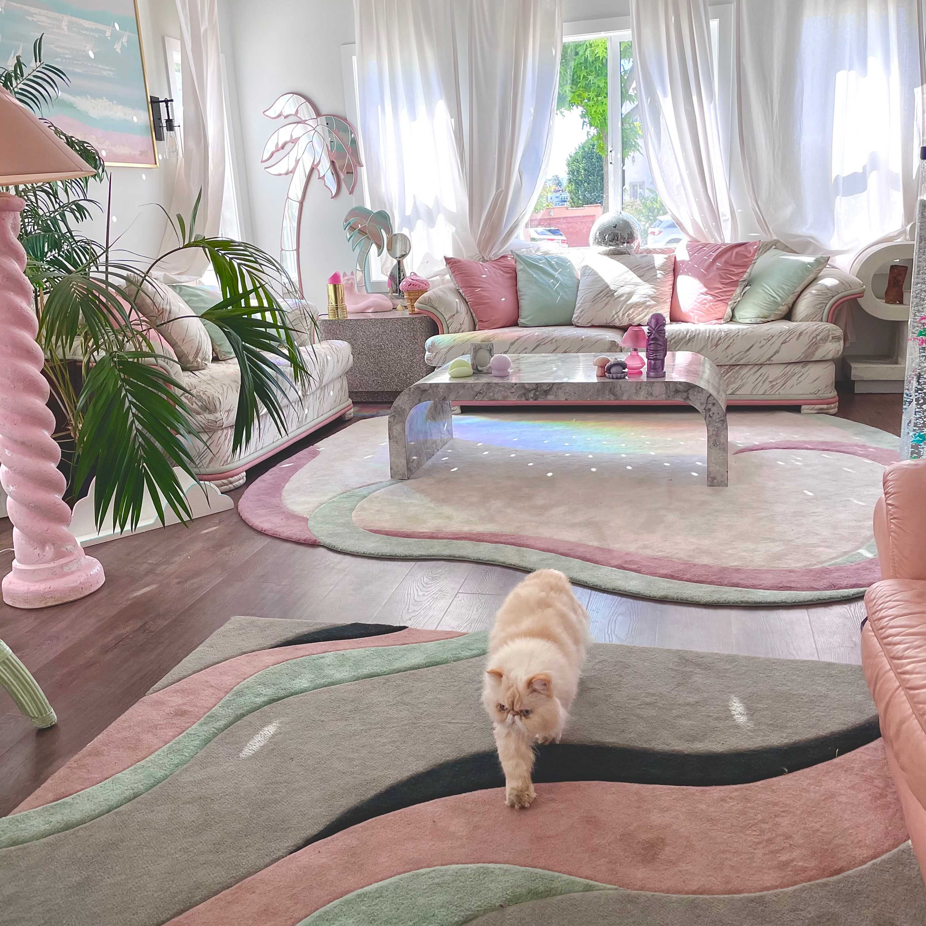 A light-filled living room features plush sofas, a modern coffee table, and a cat walking across a patterned rug.
