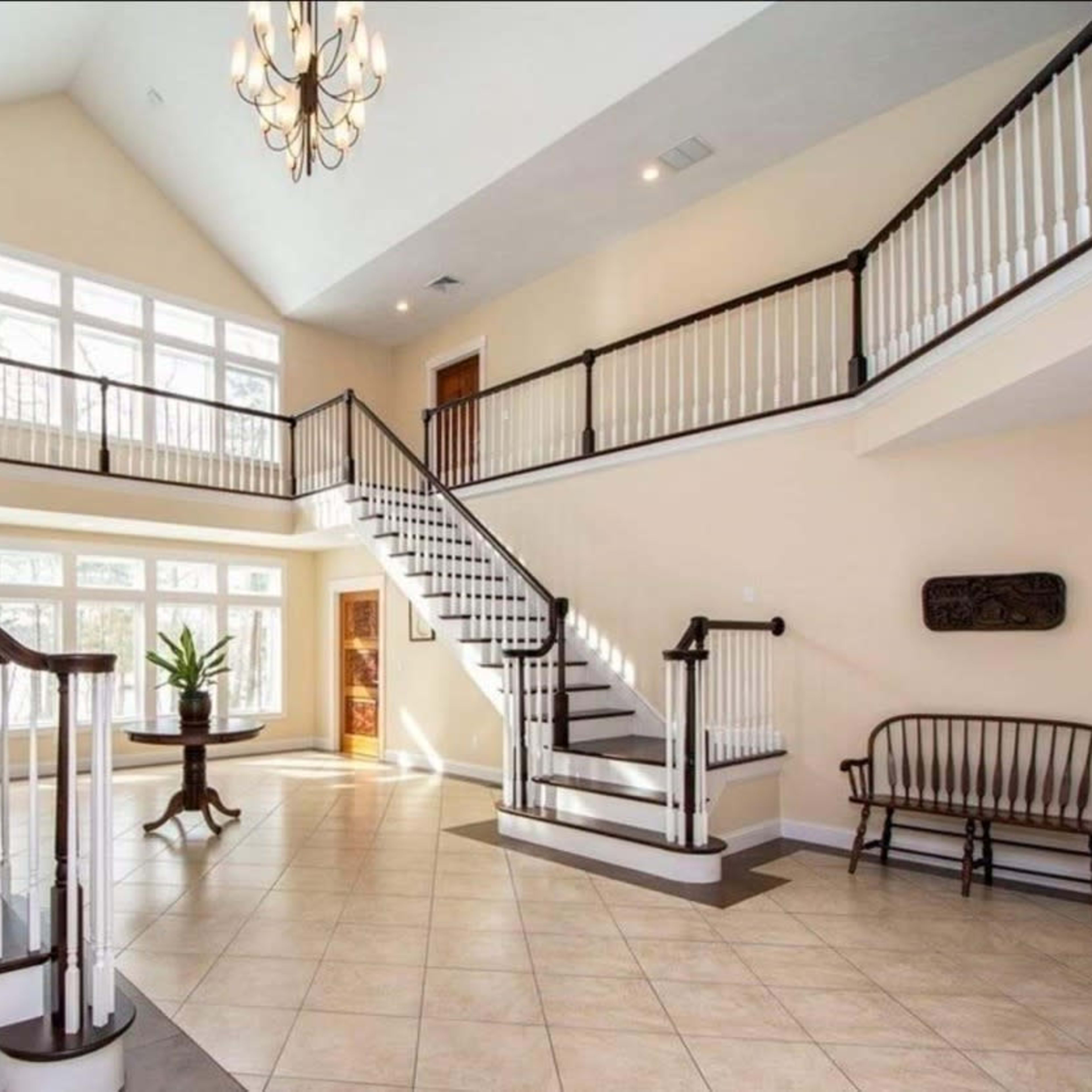 A spacious two-story entryway with large windows, sweeping staircases, and a bench by the wall.