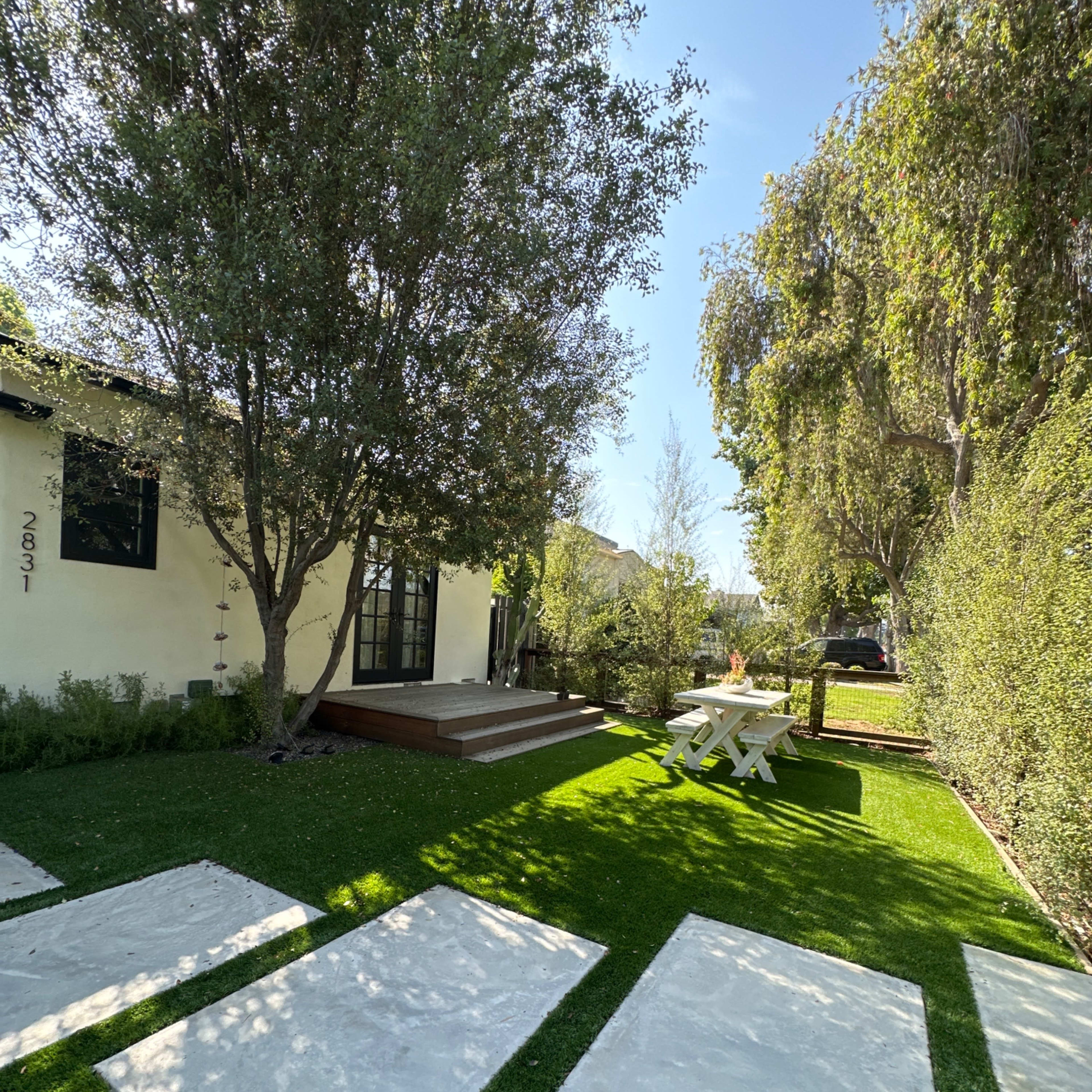 A landscaped yard with a pathway of large stone slabs leading to a house surrounded by trees and a picnic table in the grass.