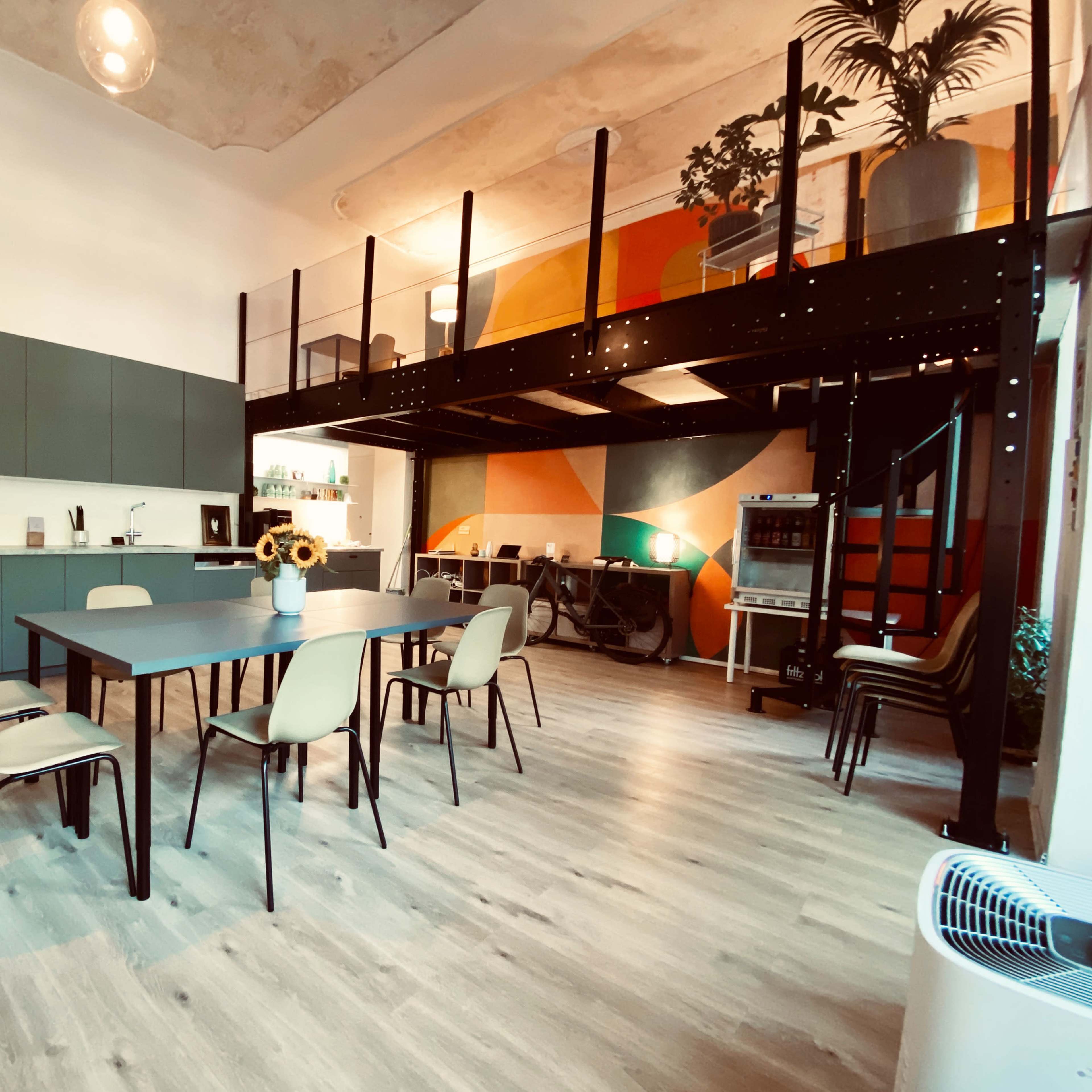 A modern open-plan kitchen and dining area with a large table and chairs, leading to a lofted space above.