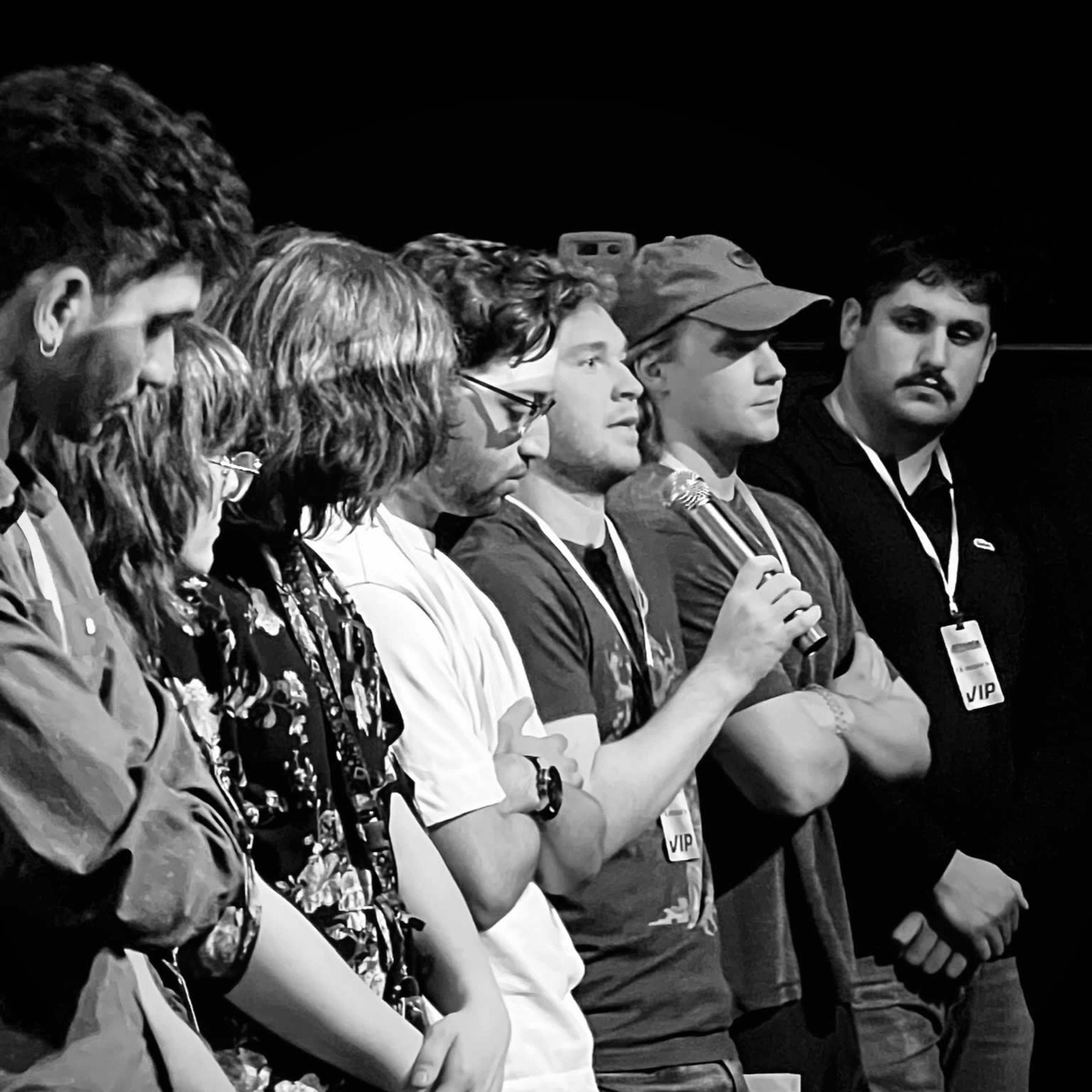 A group of individuals stands in a line on stage, with one person speaking into a microphone while the others listen attentively.
