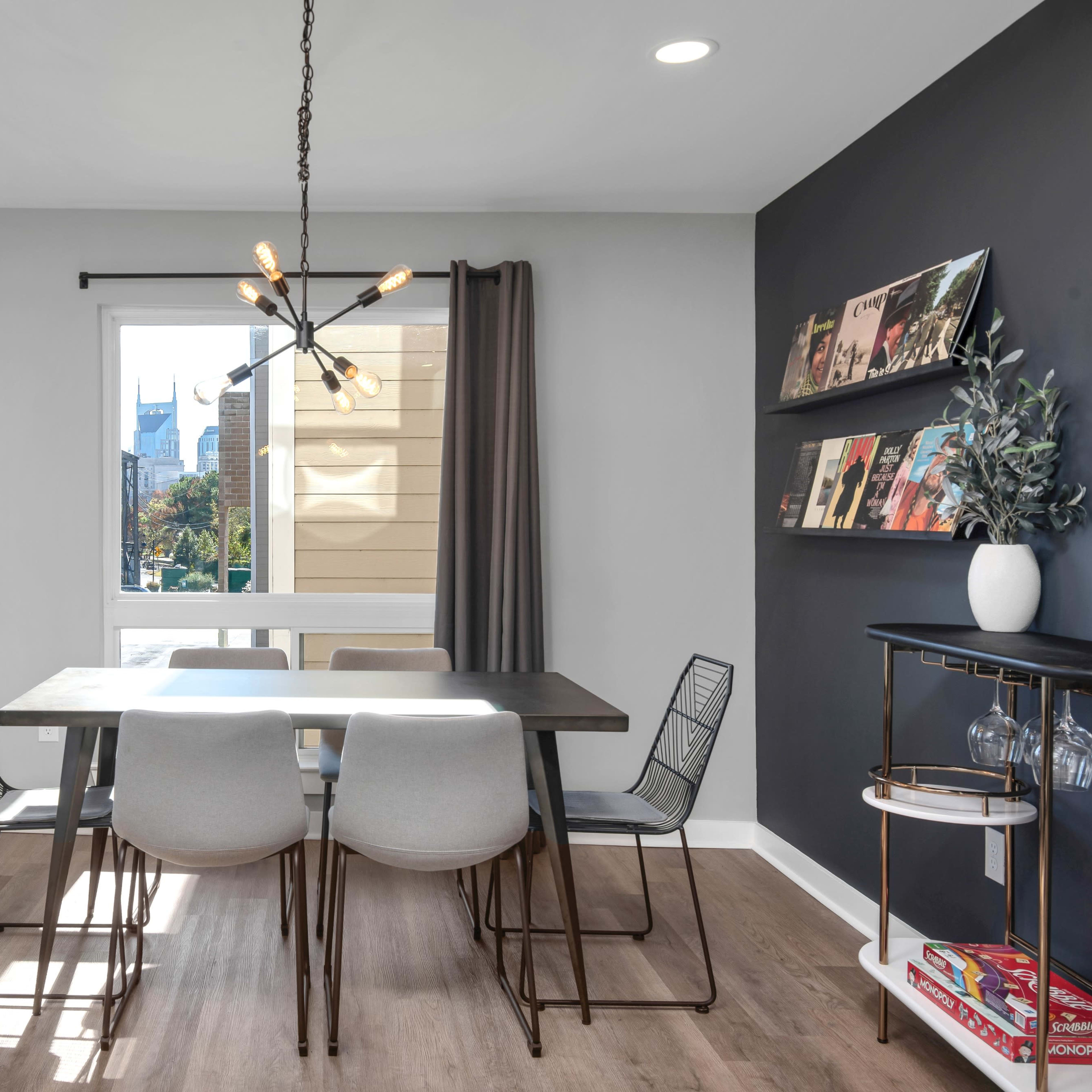 A modern dining area with a rectangular table surrounded by six chairs, a window with a view, and minimalist decor including a pendant light and wall shelves.