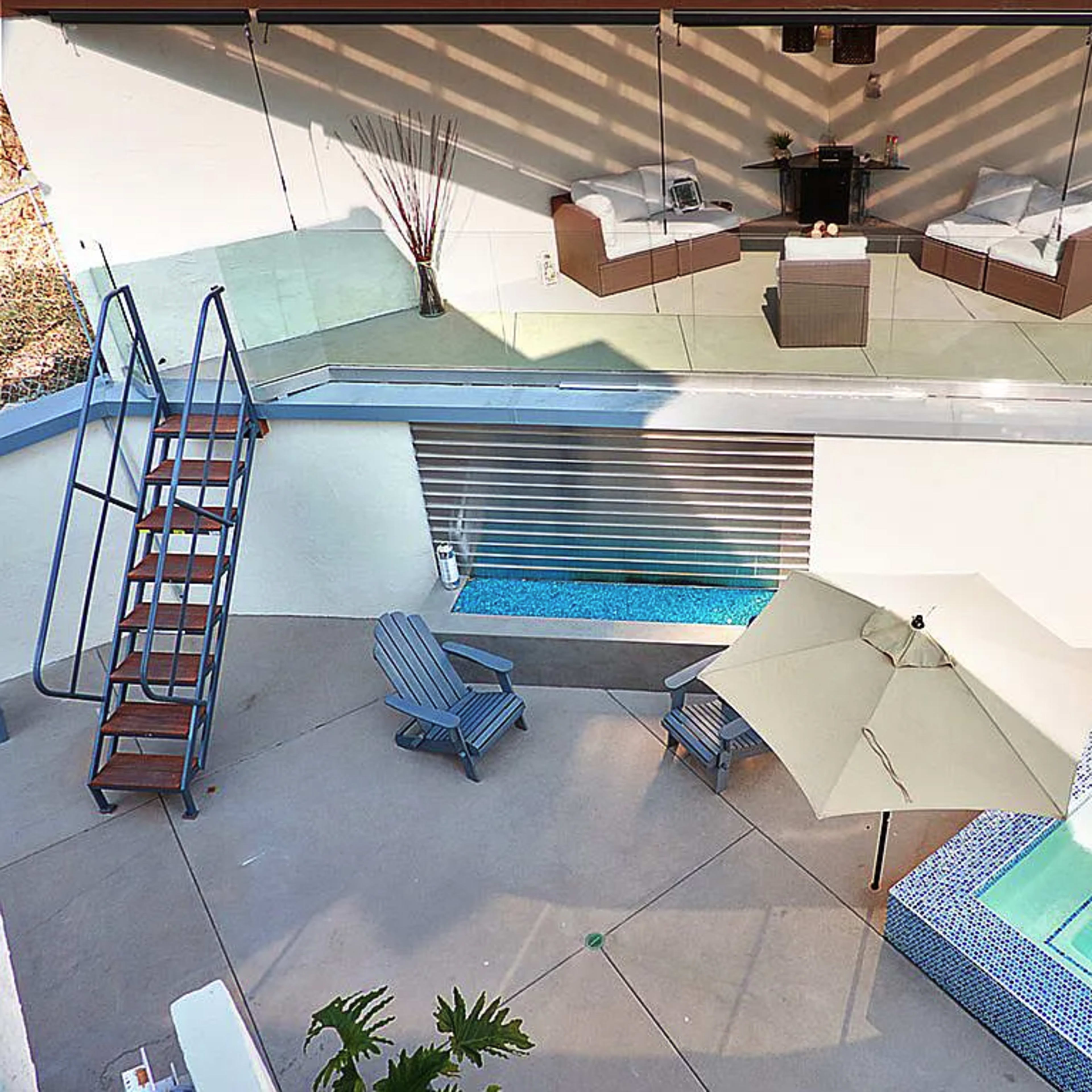 A modern outdoor space featuring a swimming pool, a hot tub, a seating area with lounge chairs, and an umbrella for shade.