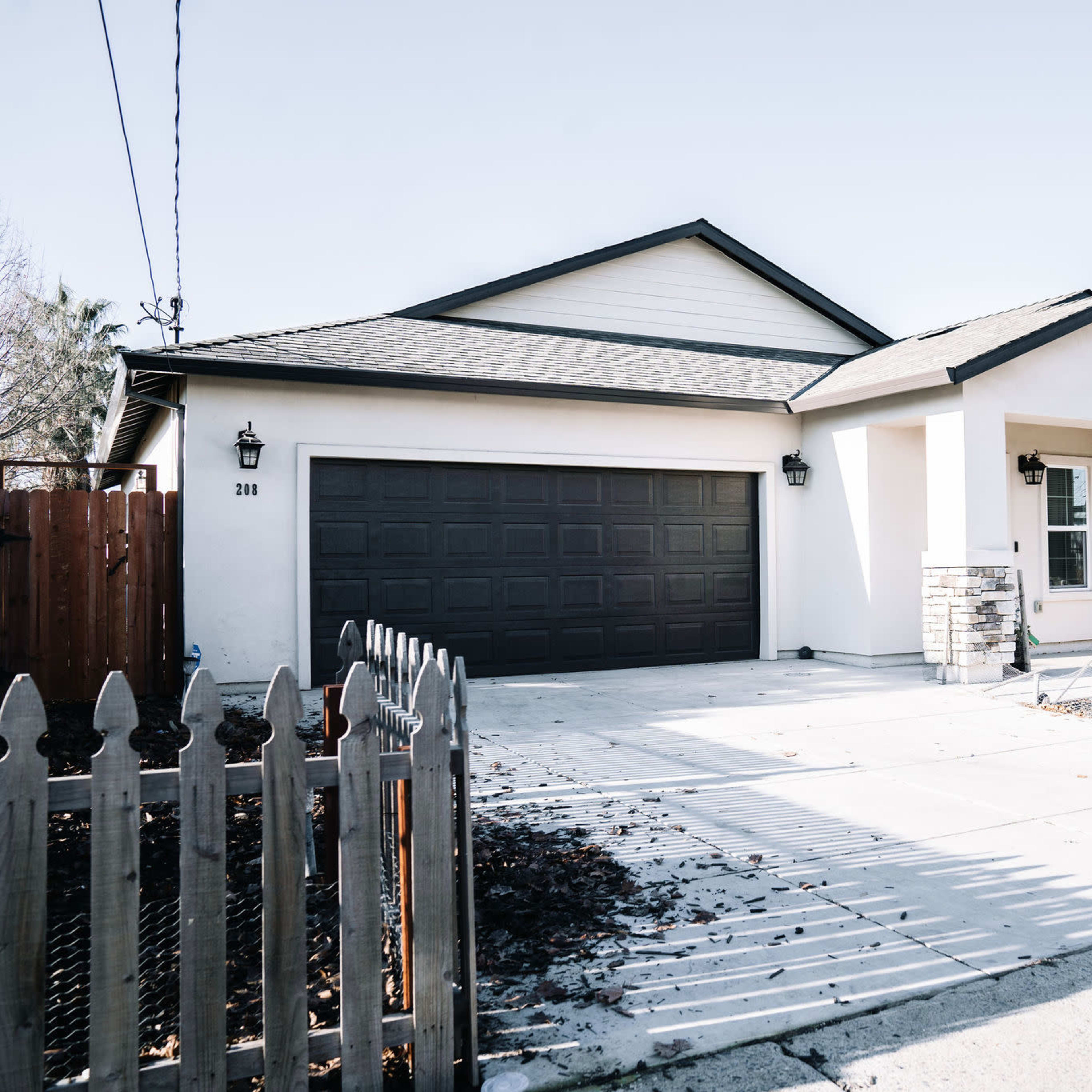 A single-story residential house with a gray garage door, a light-colored exterior, and a neatly landscaped front yard.