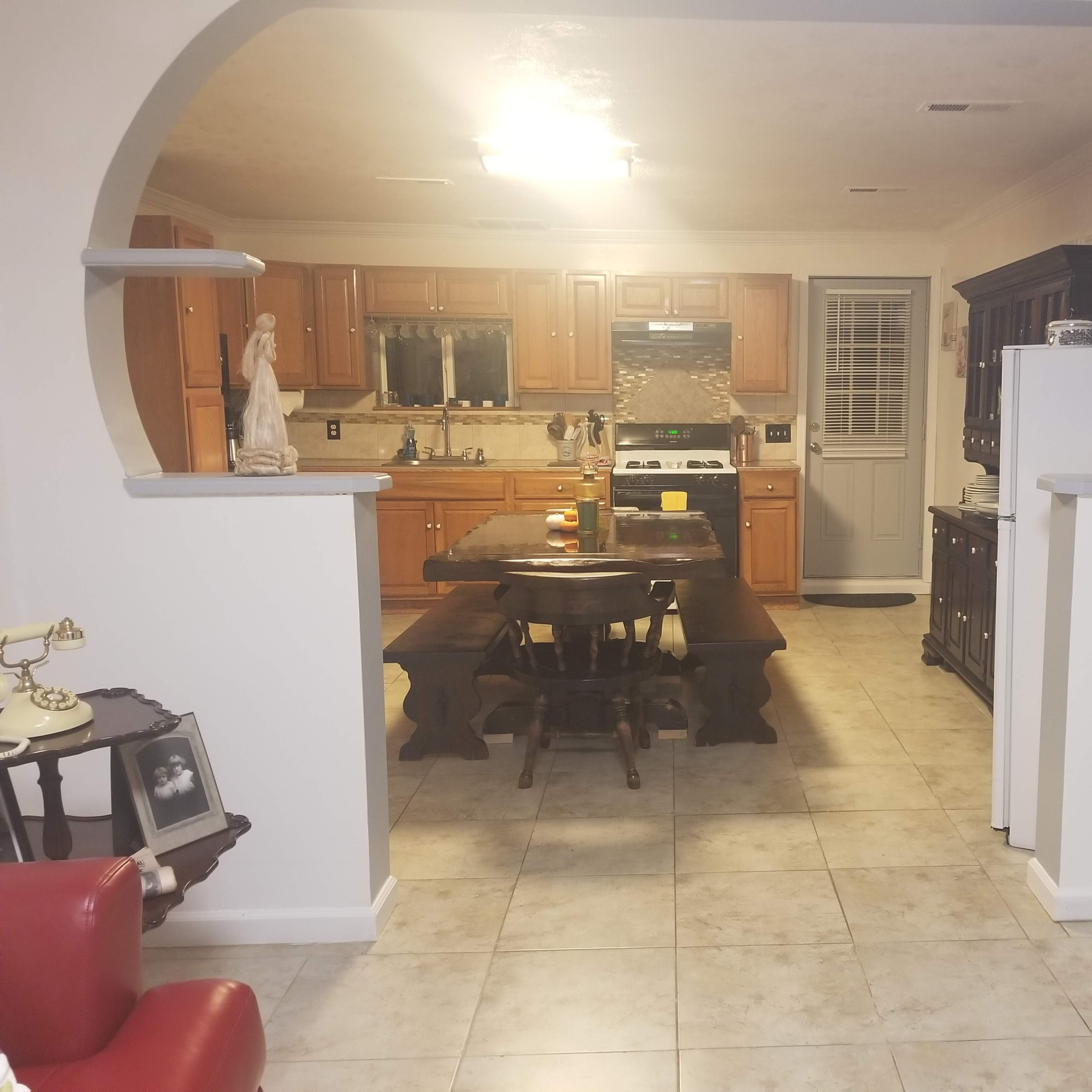 A spacious kitchen with wooden cabinets, a large dining table in the center, and a doorway leading to a side entrance.