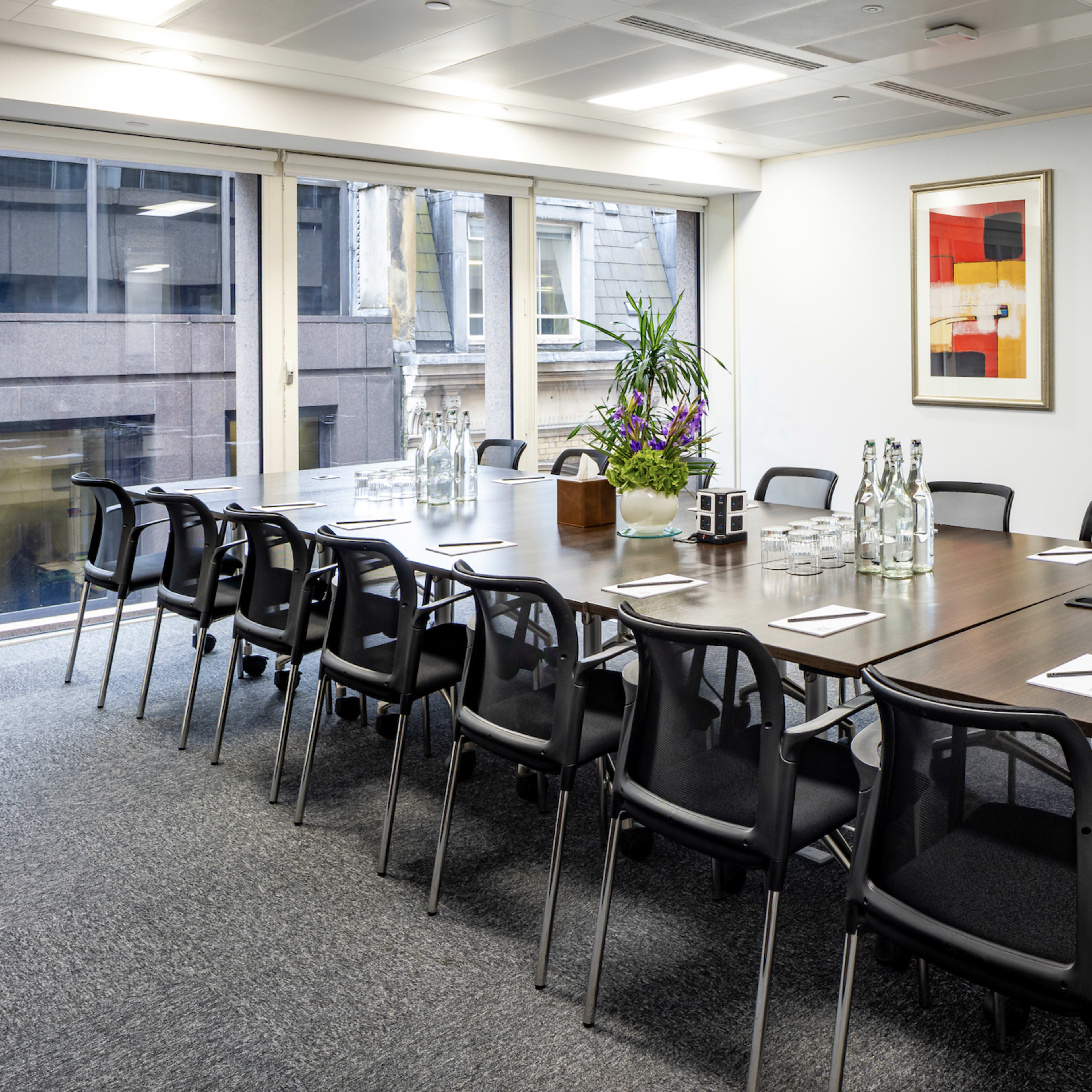 A large, modern conference room is set up for a meeting, with a long table surrounded by black chairs, glass water bottles, and artwork on the walls.