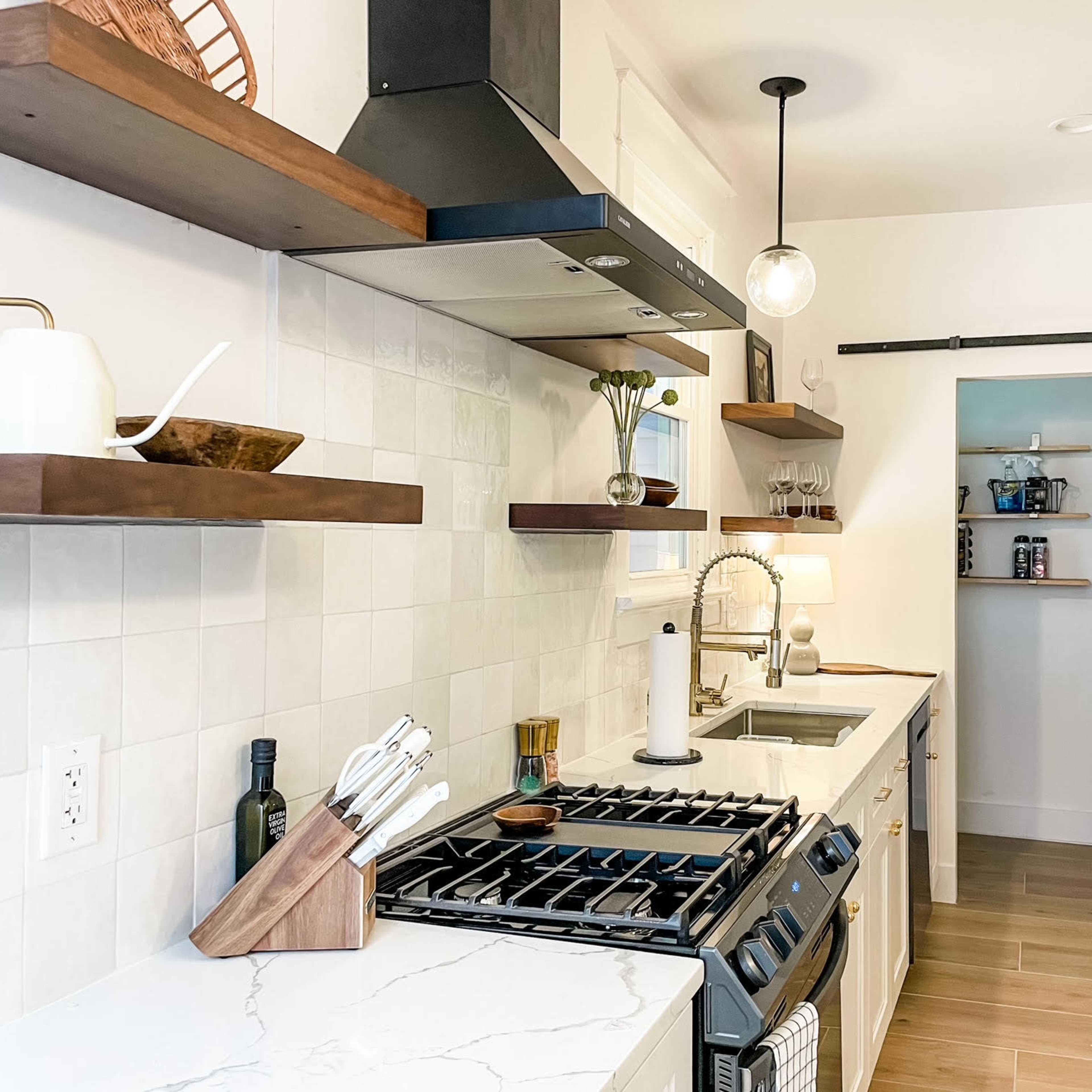 A modern kitchen features white cabinetry, wooden open shelves, a gas stove, and a sliding door to a pantry.