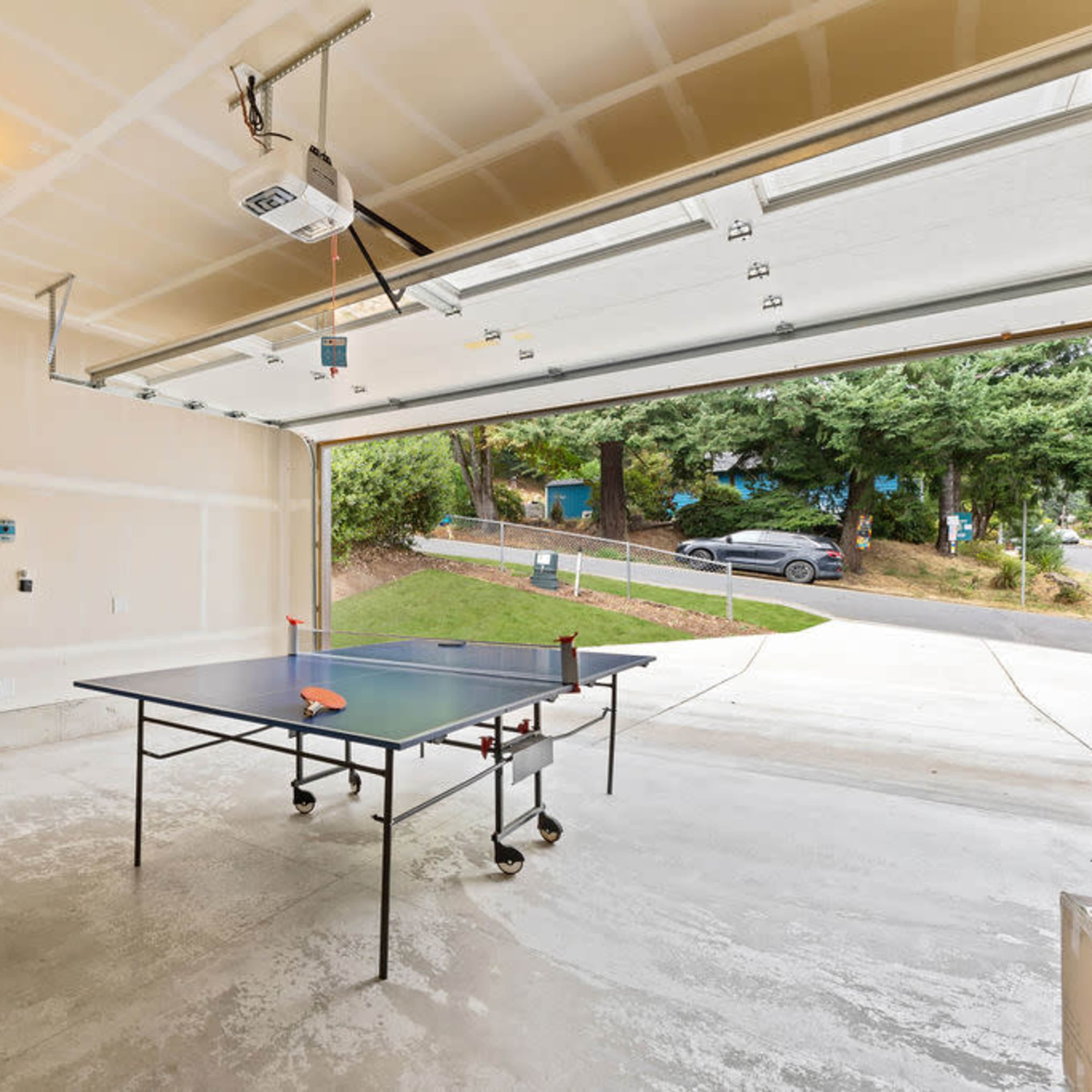 A garage with a ping pong table in the center, a step ladder, and a water heater mounted on the wall.