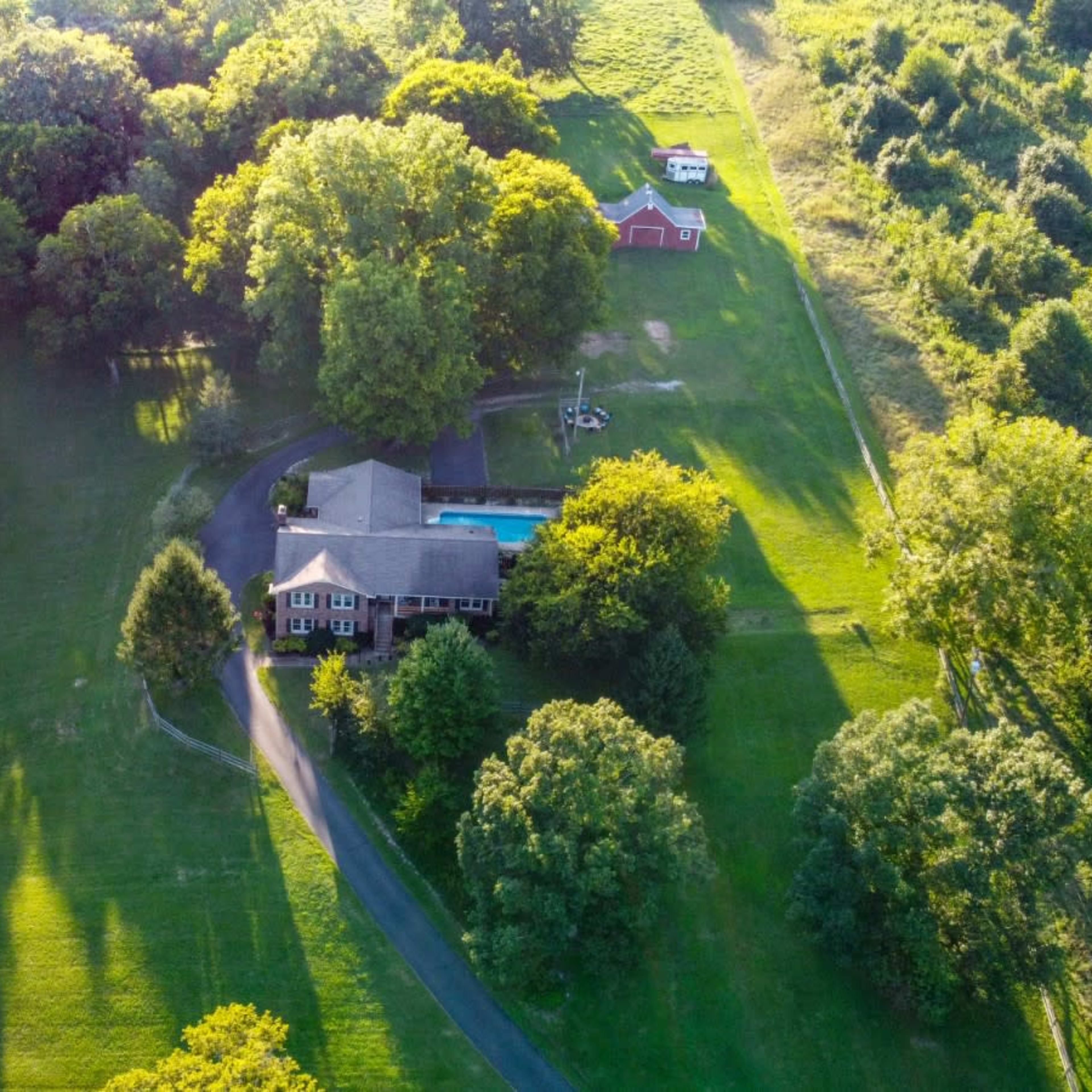 A large house surrounded by trees and grass, with a swimming pool and barn visible in the yard.