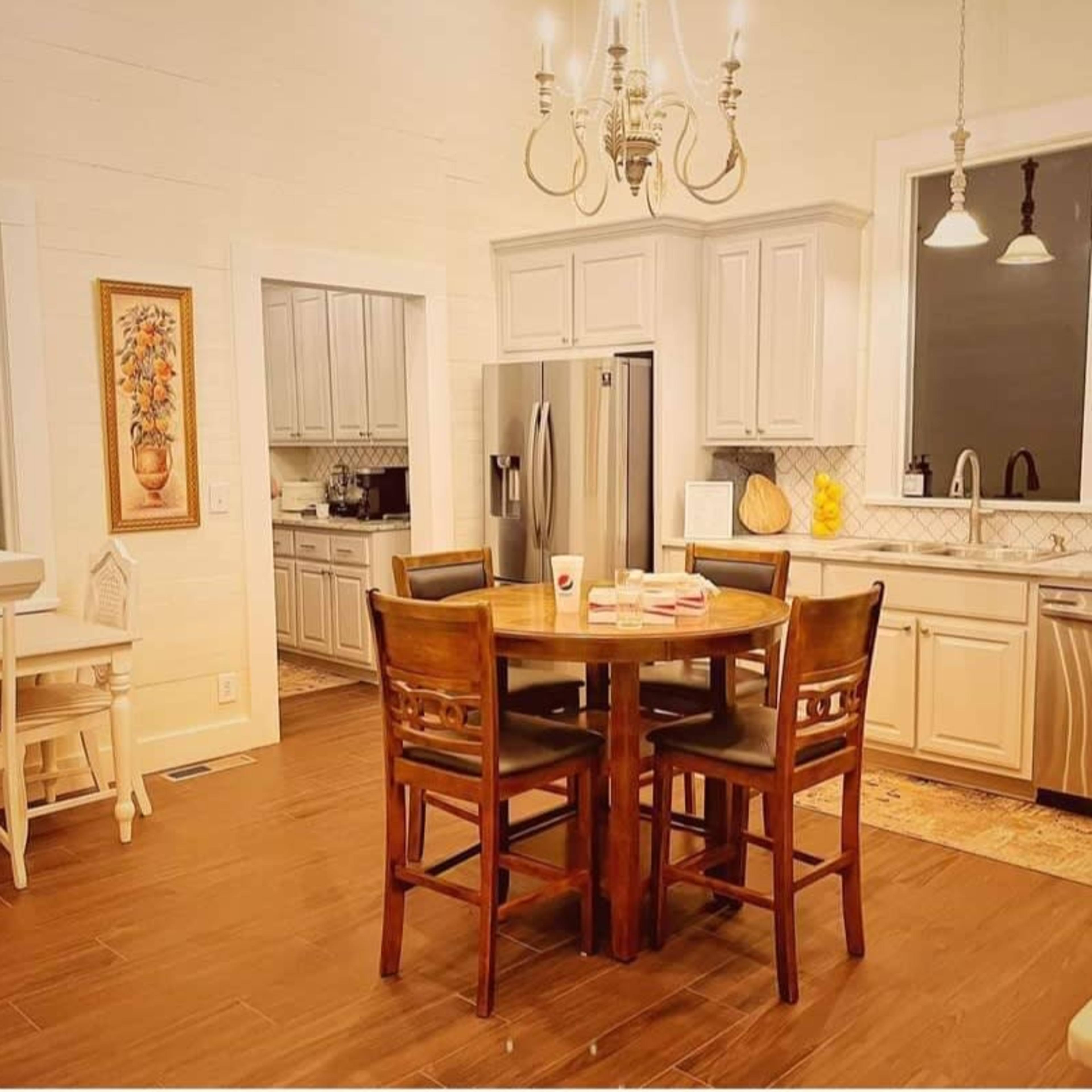 A modern kitchen featuring gray cabinets, stainless steel appliances, a round wooden dining table with four chairs, and a chandelier above.