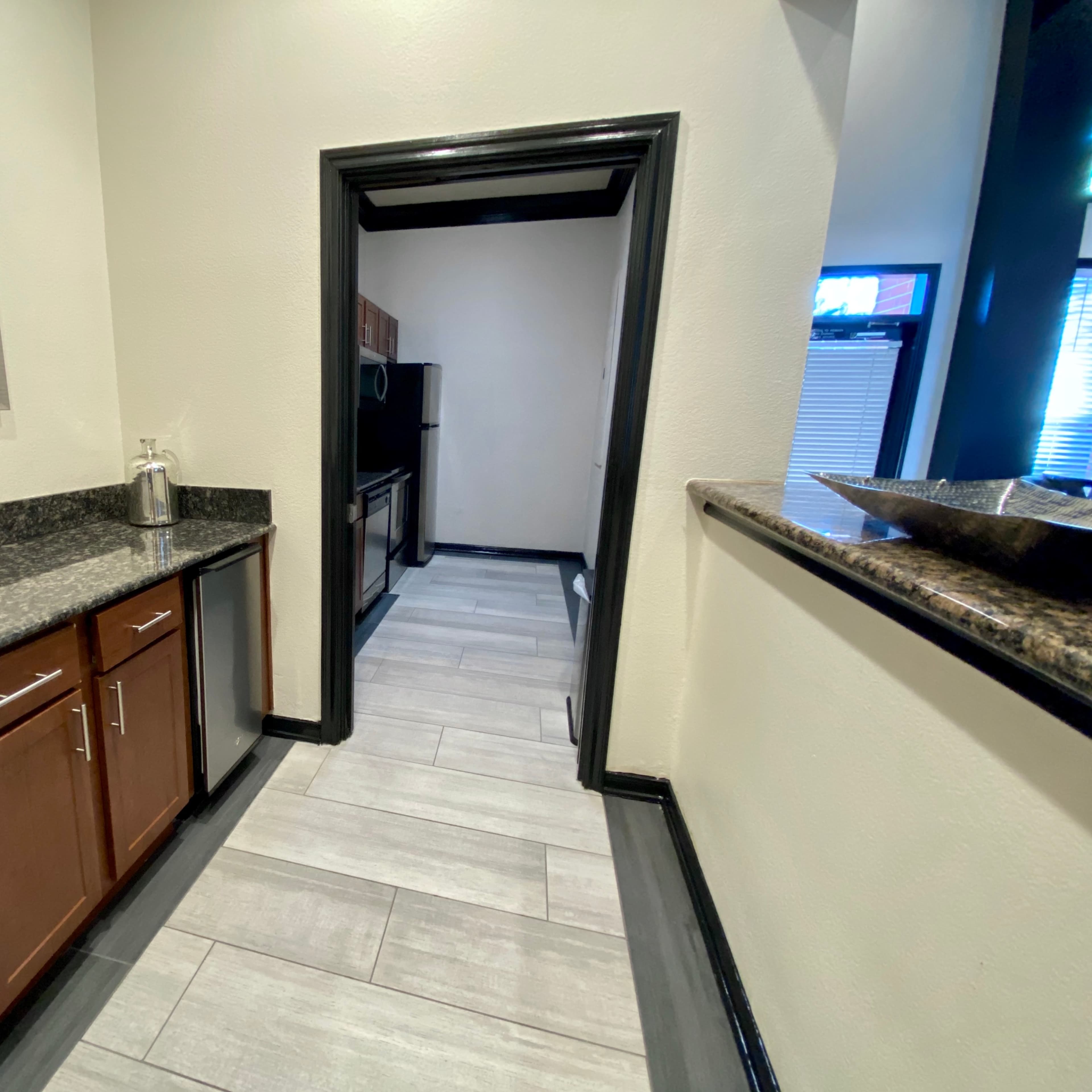 A hallway leading to a kitchen, with wooden cabinets and dark granite countertops along one side.