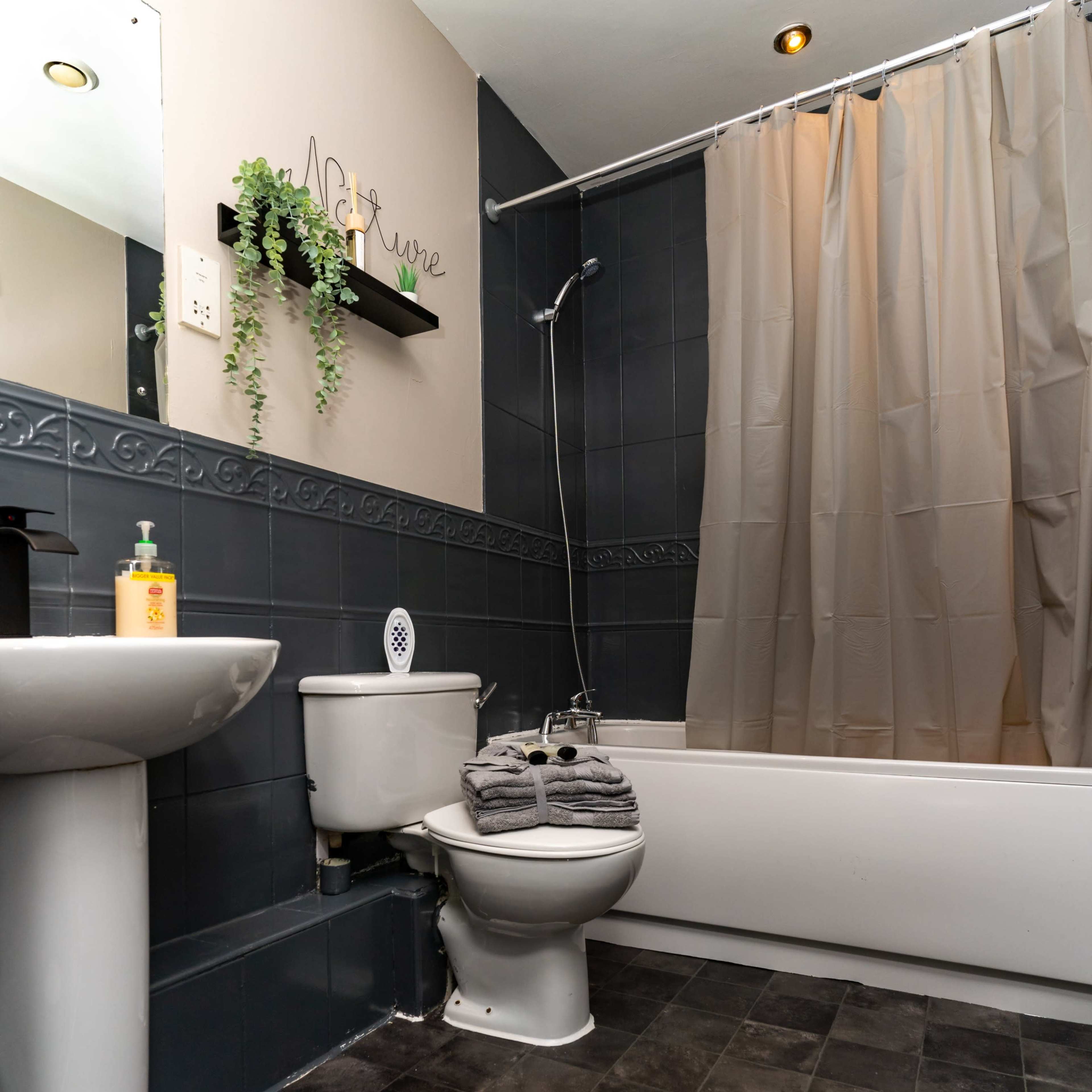 A bathroom featuring a bathtub, shower, toilet, sink, and a decorative shelf with a plant.