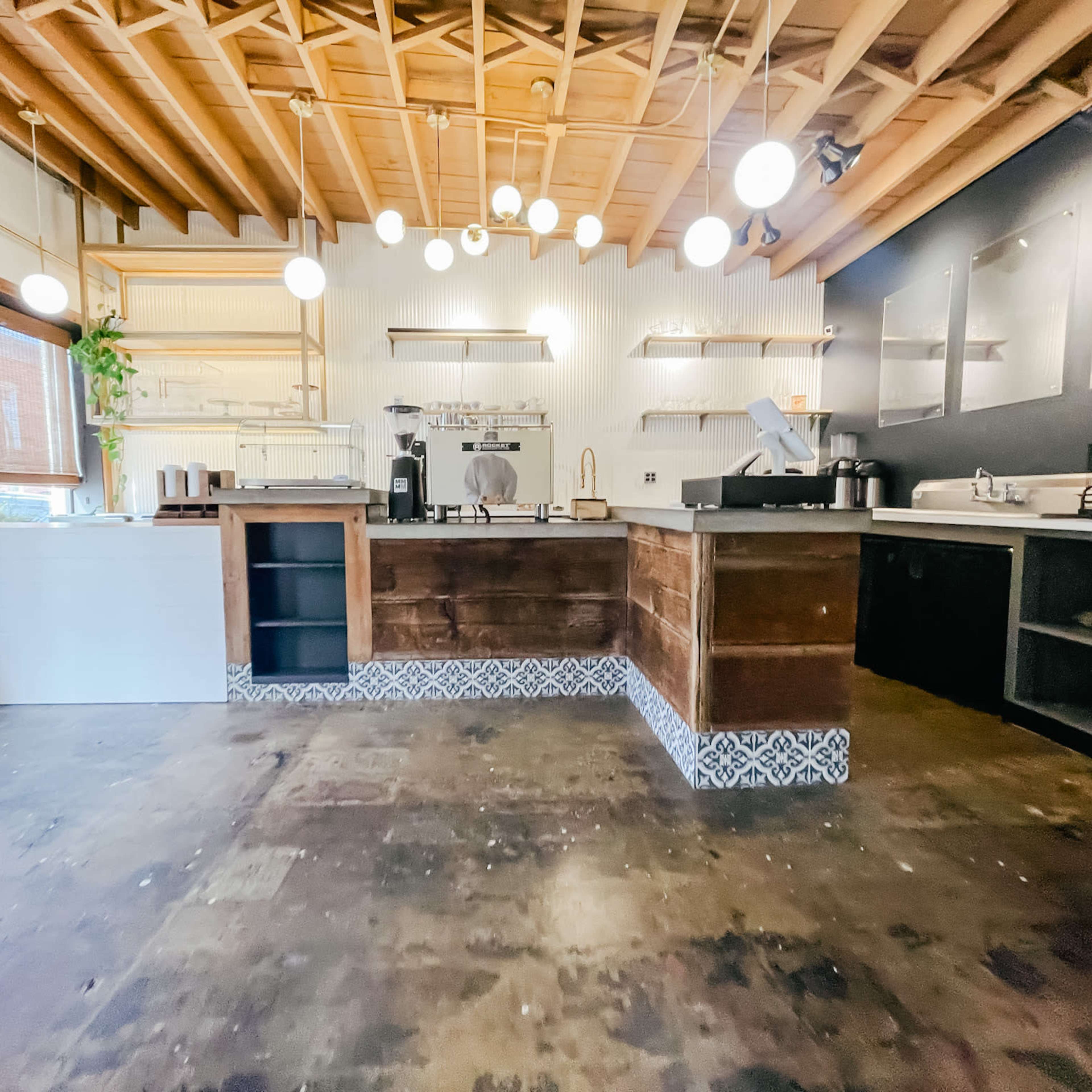 A modern café interior with wooden cabinetry, pendant lighting, and a polished floor featuring a patterned tile border.