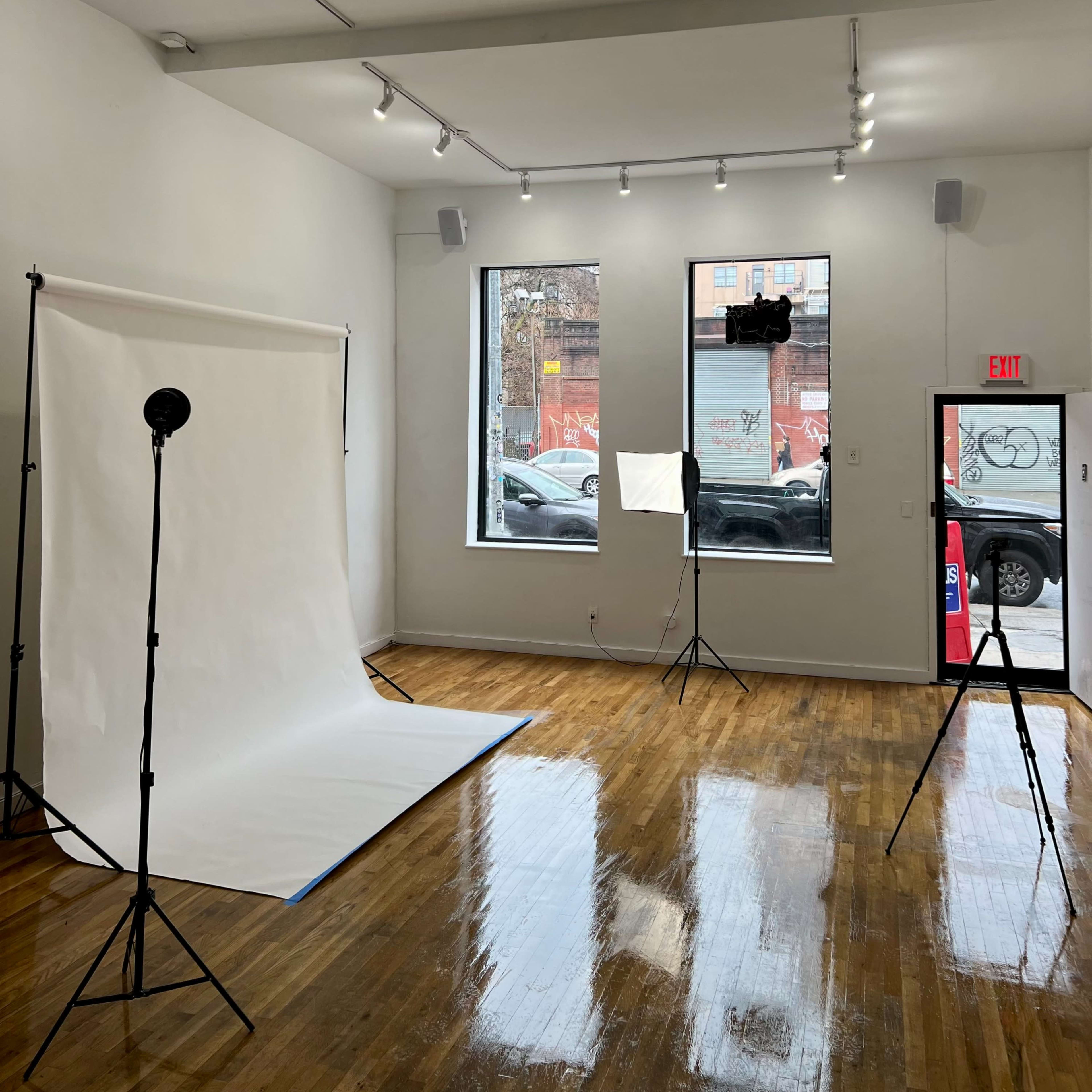 A bright photography studio with a backdrop, lighting equipment, and large windows.