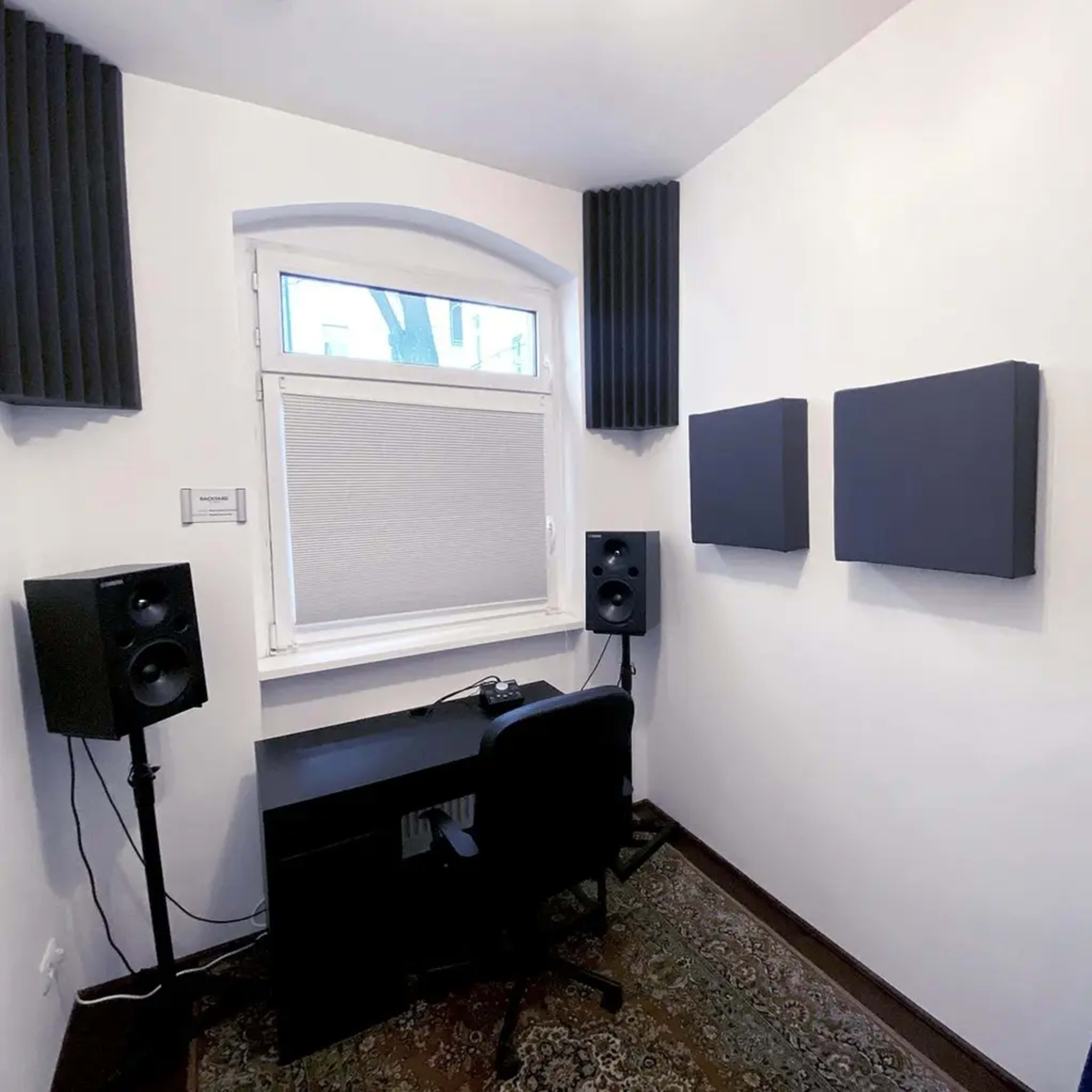 A small recording studio with soundproofing panels on the walls, a desk with a chair, and speaker monitors placed on either side.