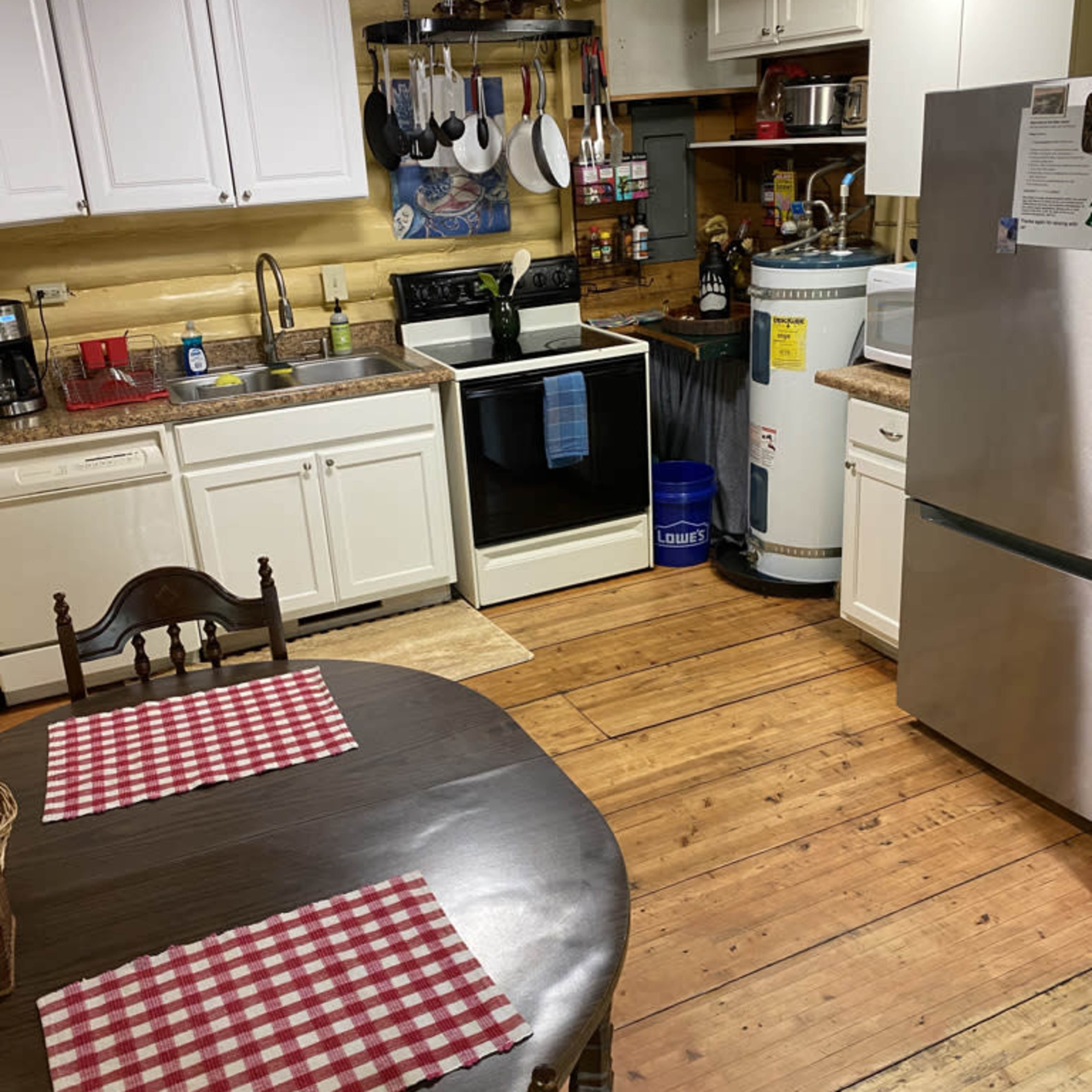 A kitchen with white cabinets, a black stove, a stainless steel refrigerator, and a wooden table set with checkered placemats.