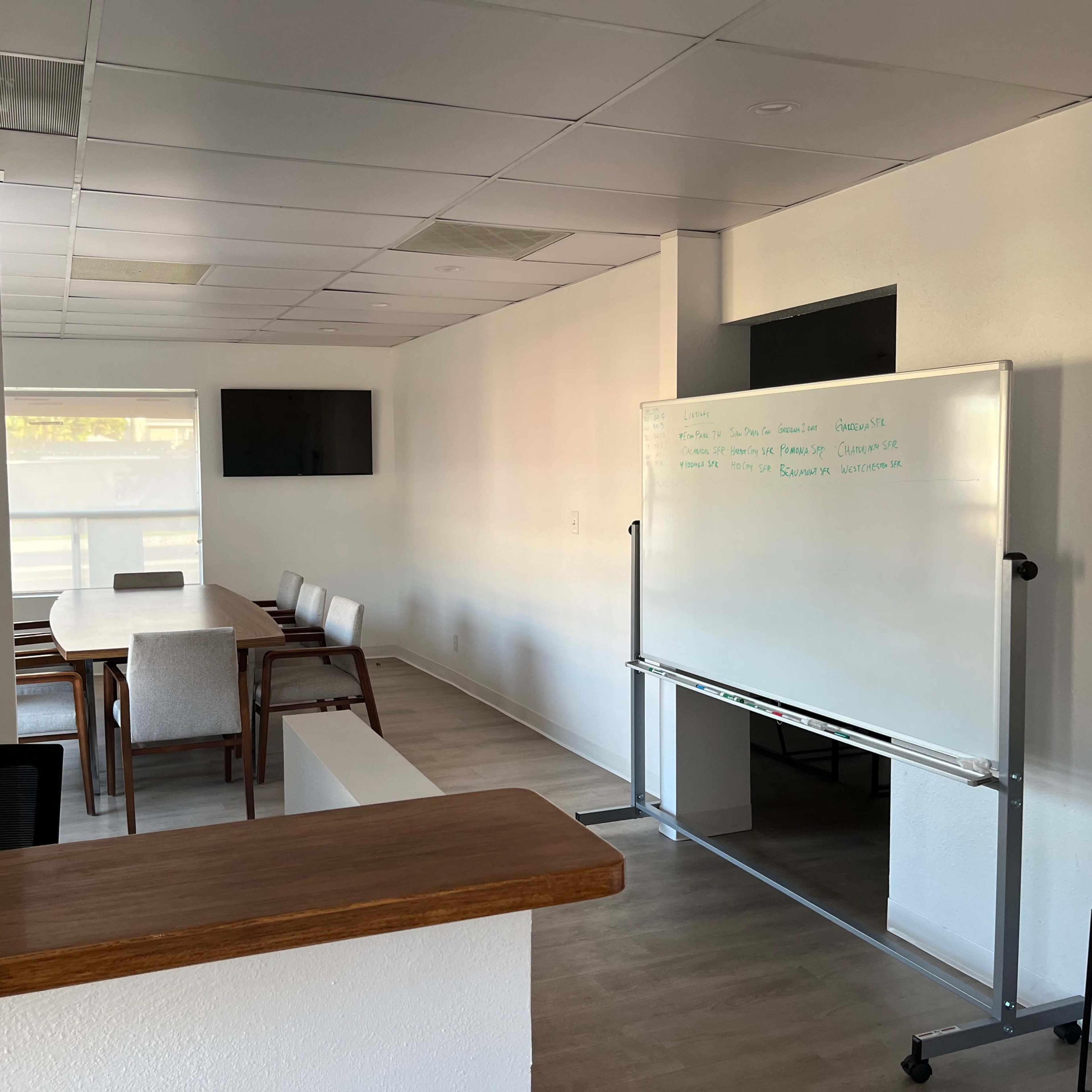 A modern office space with a conference table, whiteboard, and a large screen on the wall.
