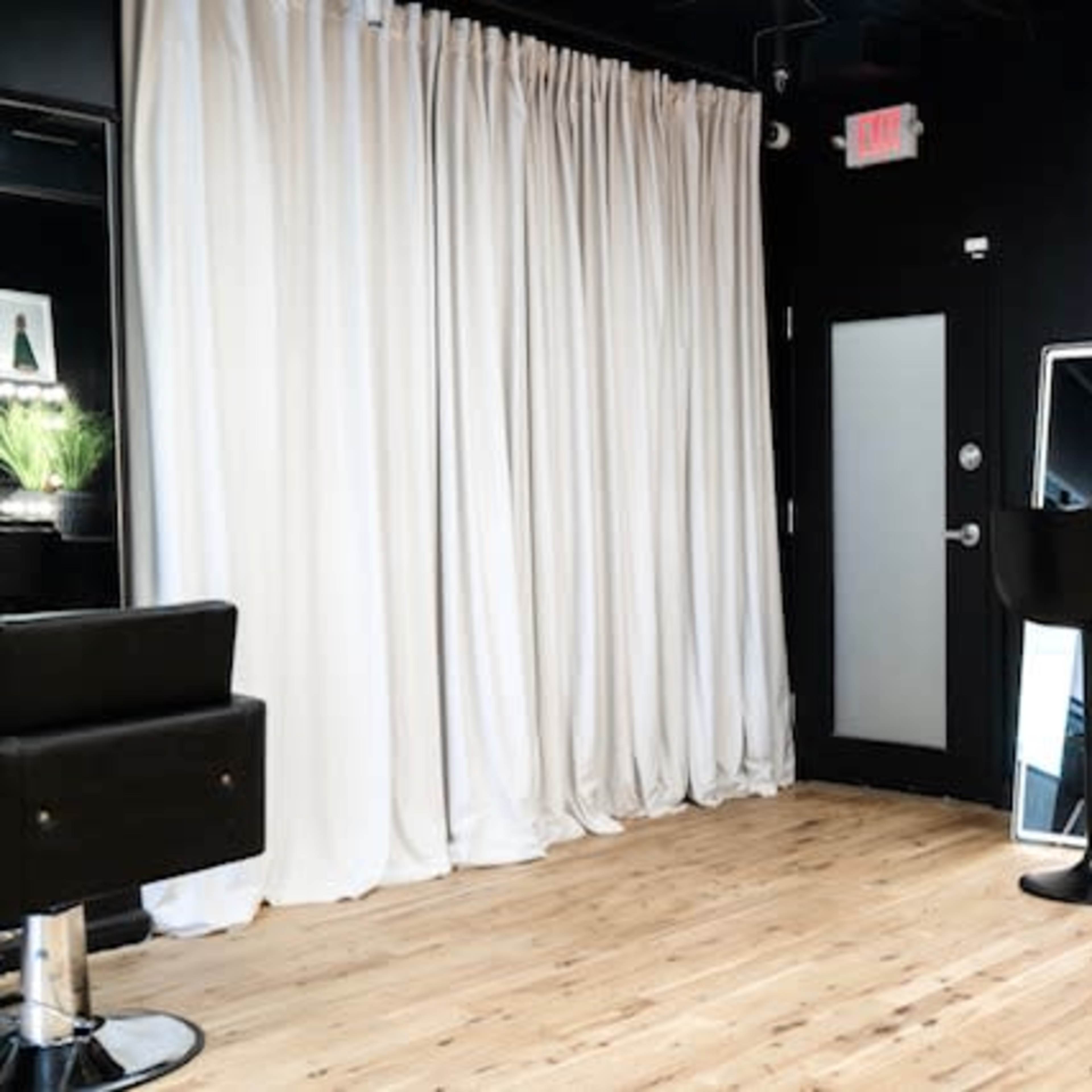 A minimalist interior with a black wall, wood floor, a large mirror, and two bar stools next to a small counter.