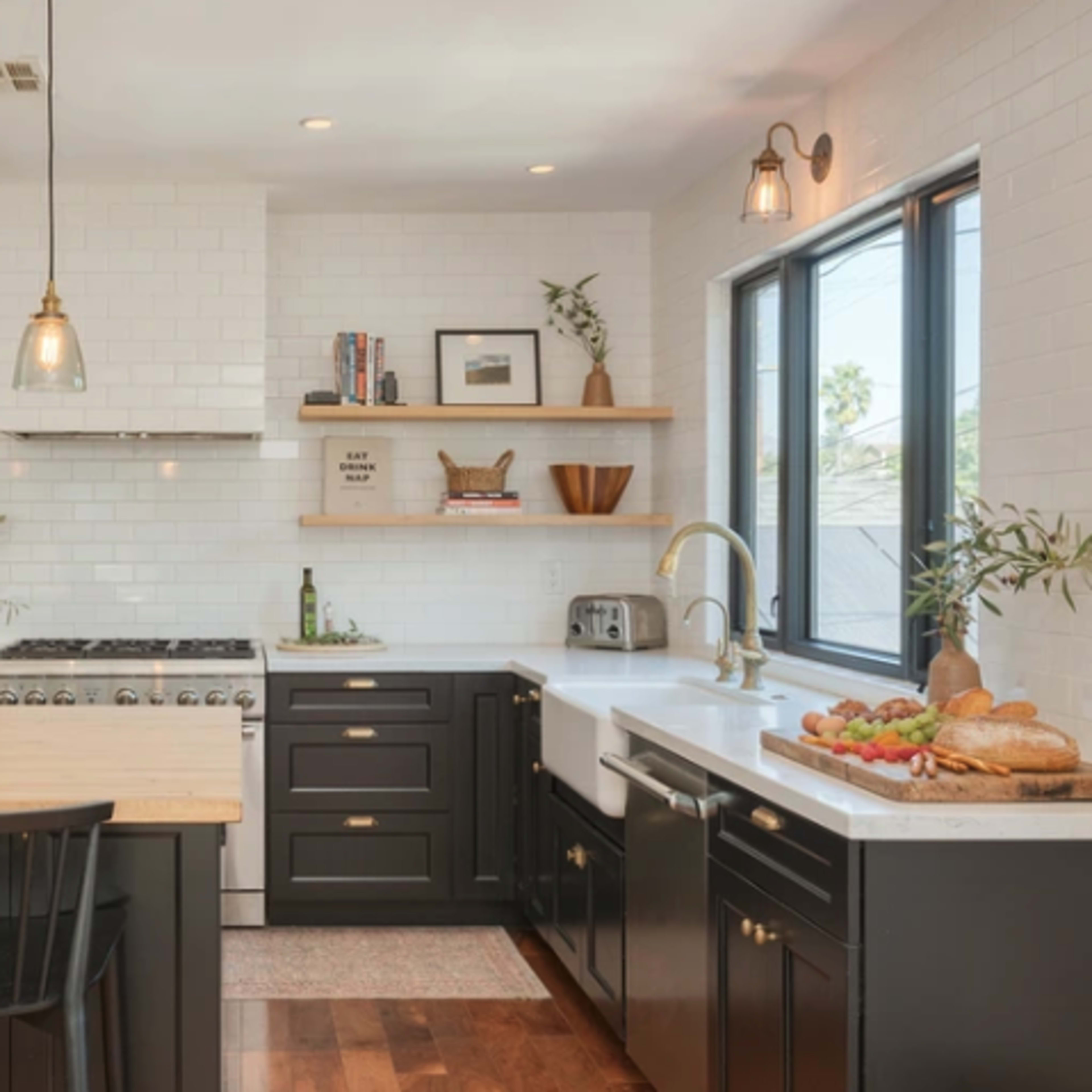 A modern kitchen featuring black cabinets, a large wooden island, stainless steel appliances, and white tile backsplash.