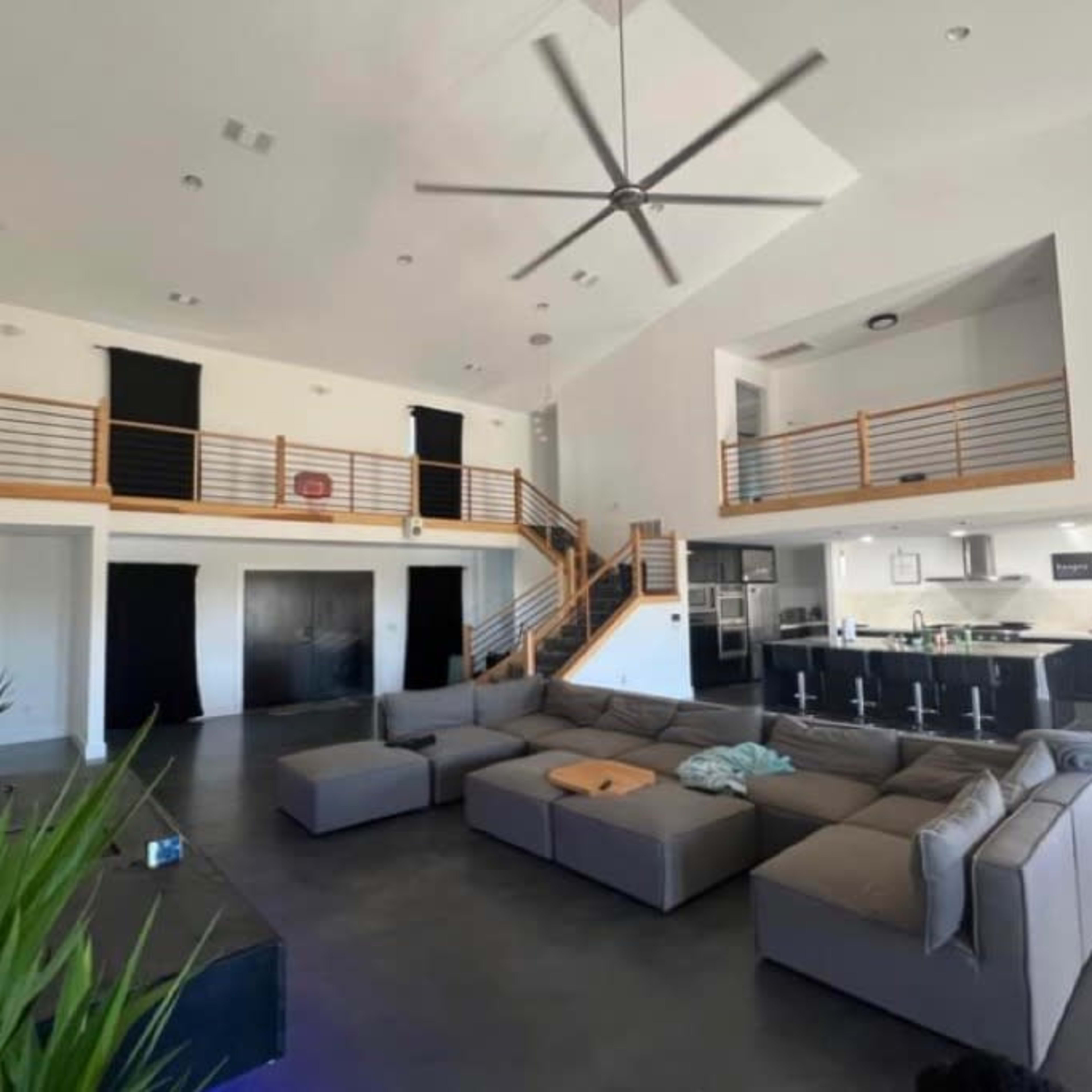 A spacious living room with a large sectional sofa, a balcony overlooking the main area, and a modern kitchen in the background.