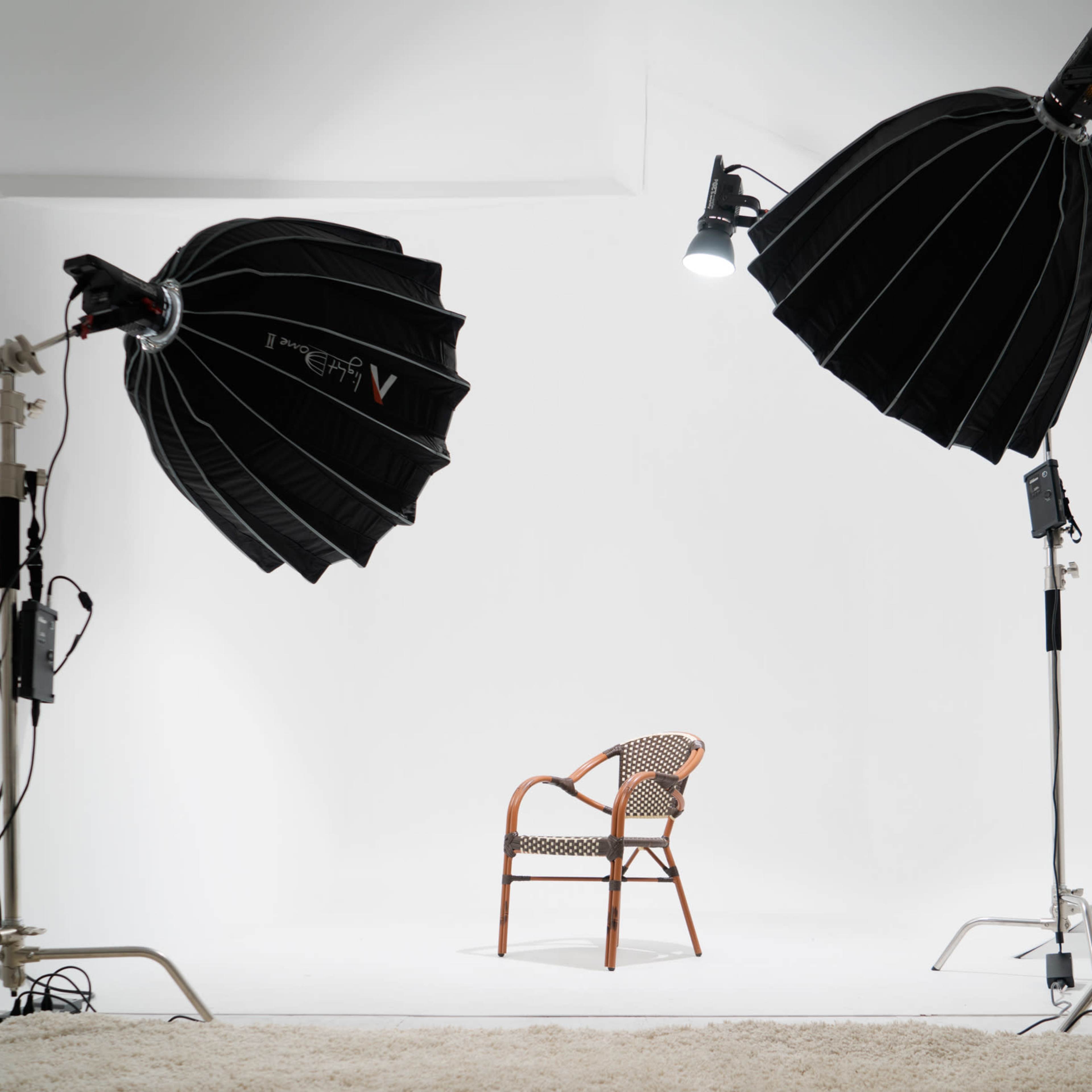 A photography studio is set up with two softbox lights illuminating an empty chair on a white backdrop.