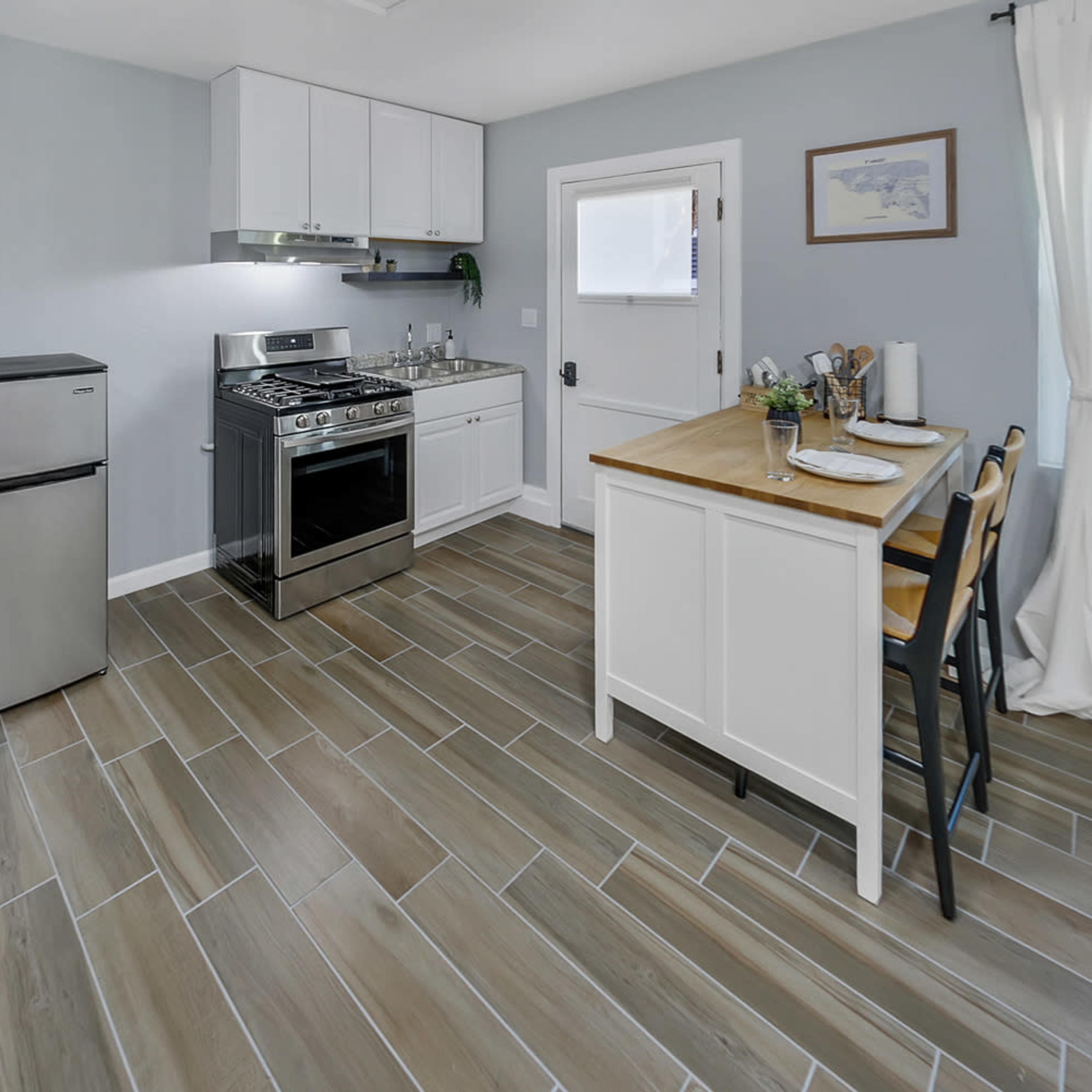 A small, modern kitchen featuring stainless steel appliances, a wooden countertop with two place settings, and light-colored walls.