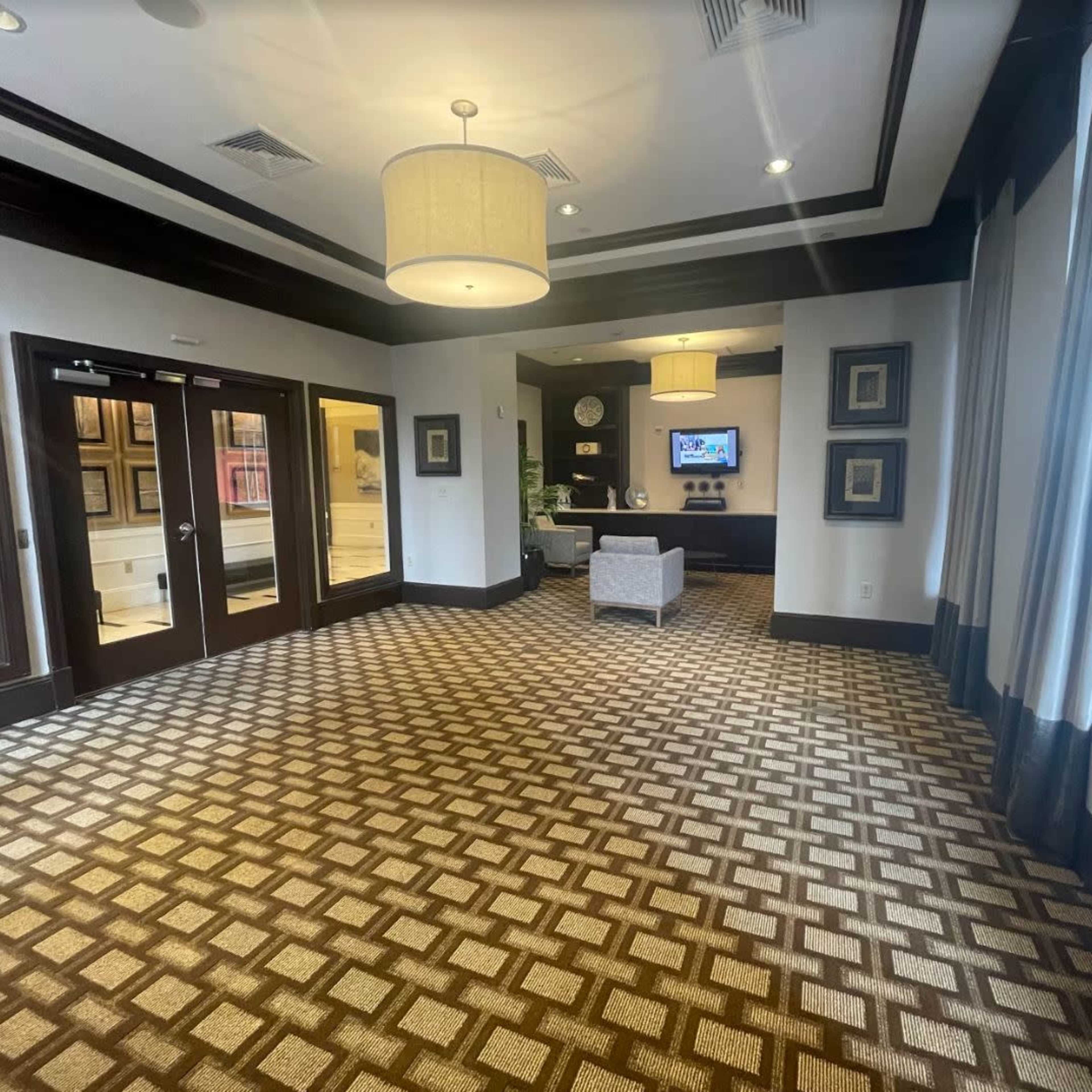 A spacious hotel lobby with patterned carpet, a seating area, and large windows letting in natural light.