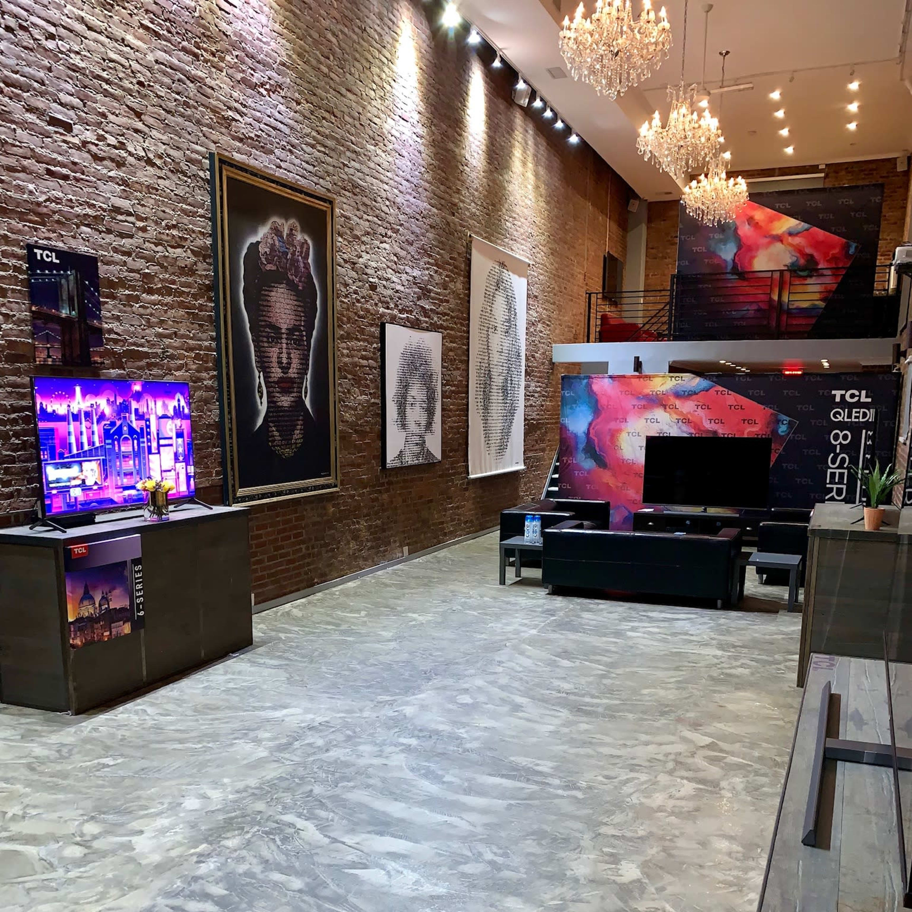 A modern showroom with a polished concrete floor, featuring various large artworks on the brick walls and multiple television displays.