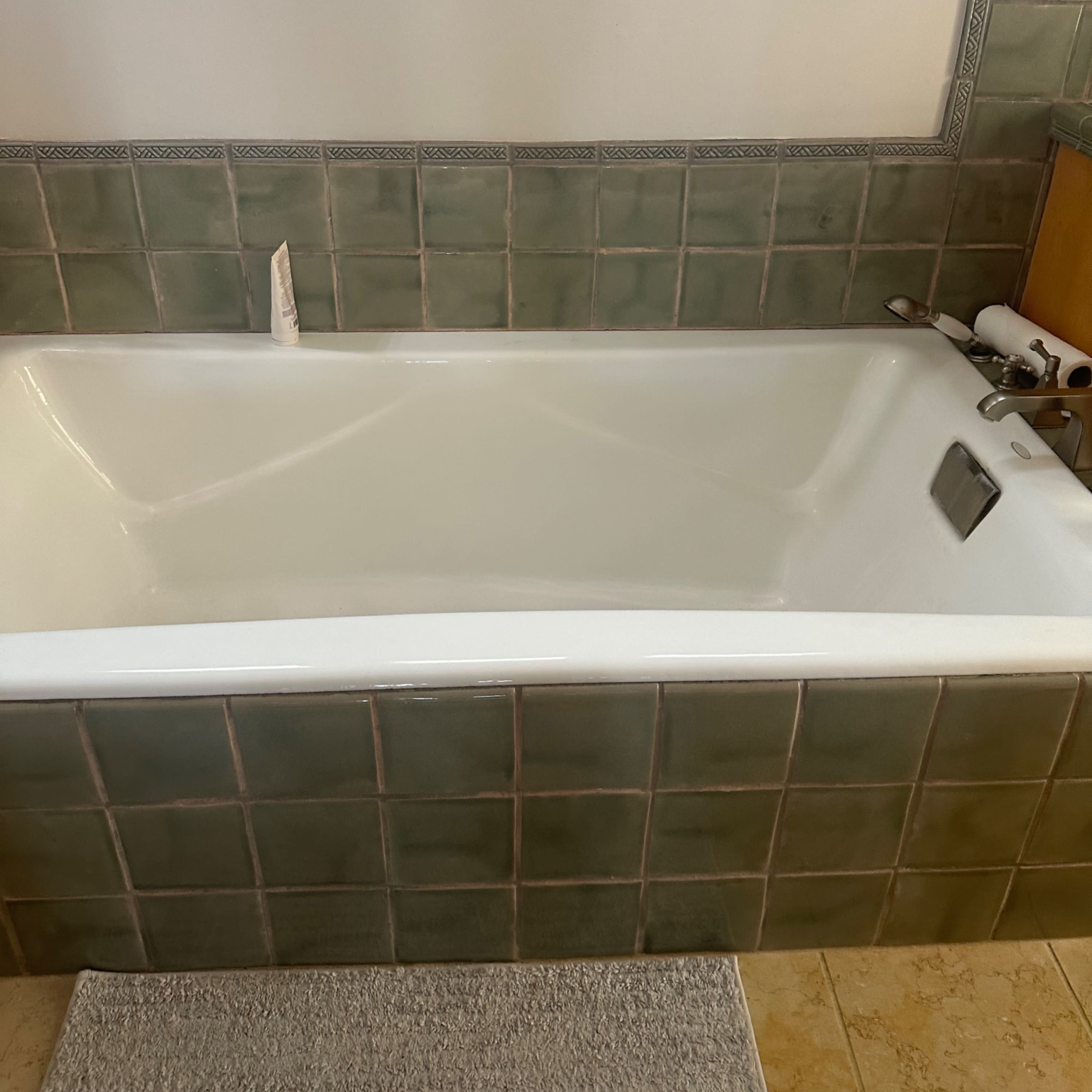 A white bathtub set against green tiled walls, with a towel rack above and bath accessories nearby.