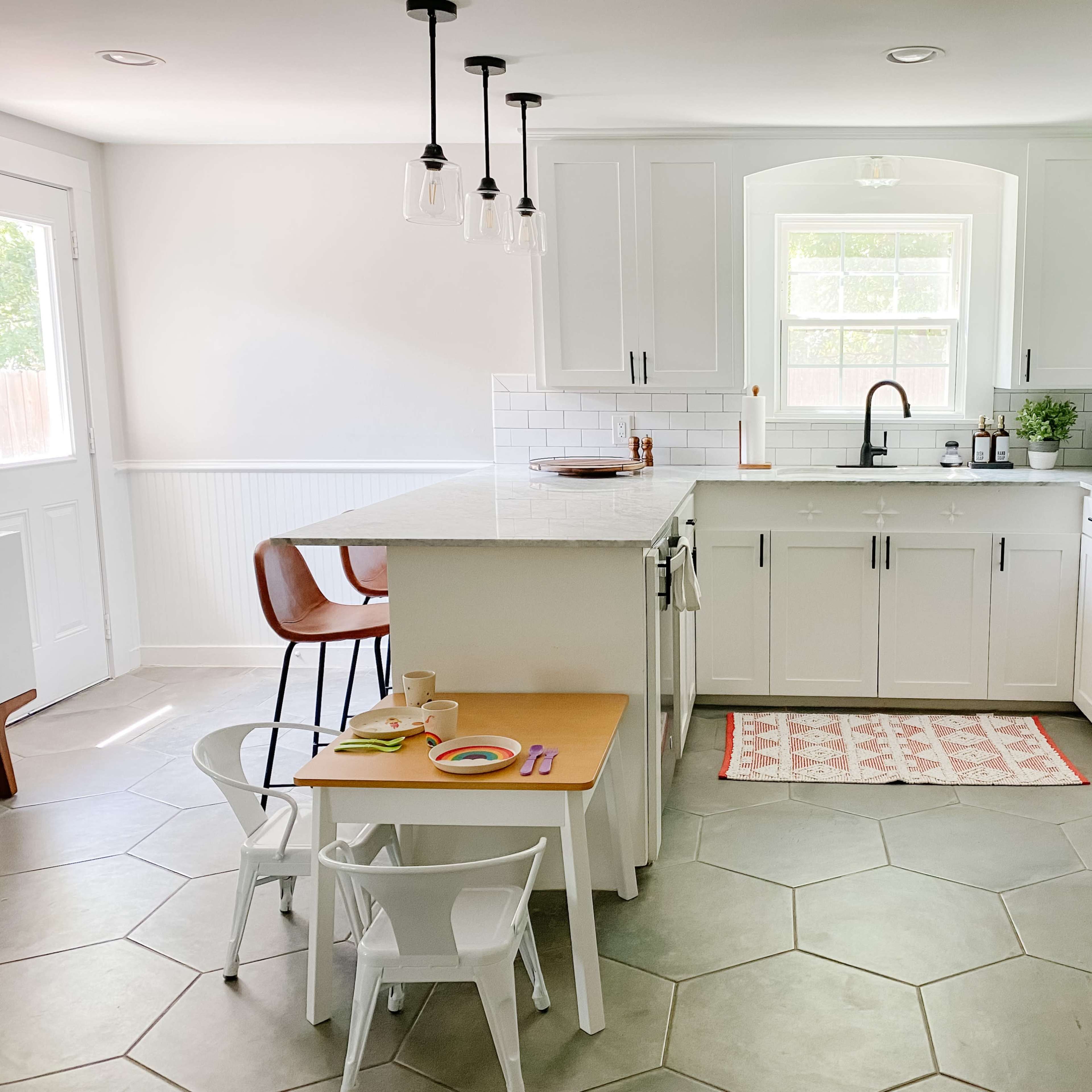 A modern kitchen featuring white cabinets, a central island, and a small table with chairs for children.