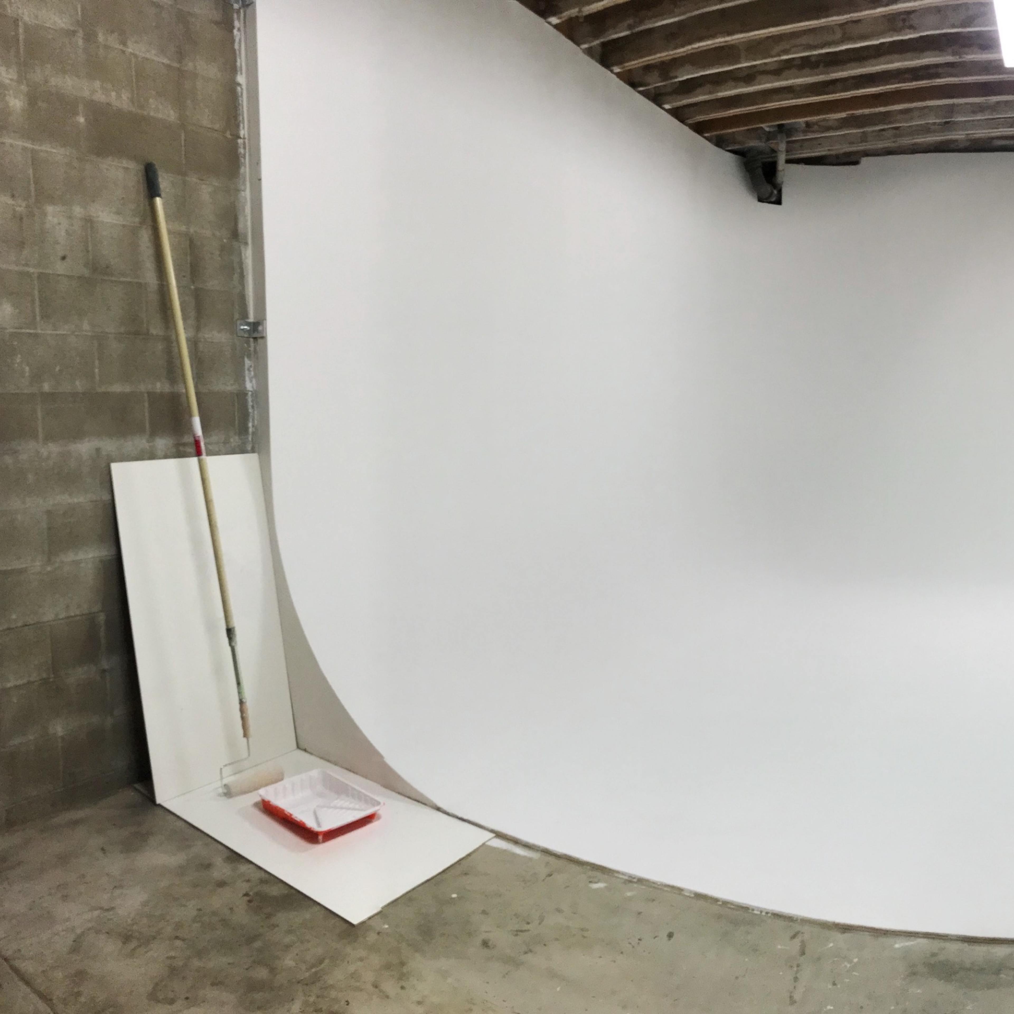 A spacious, empty photo studio with a seamless white backdrop and exposed wooden beams on the ceiling.