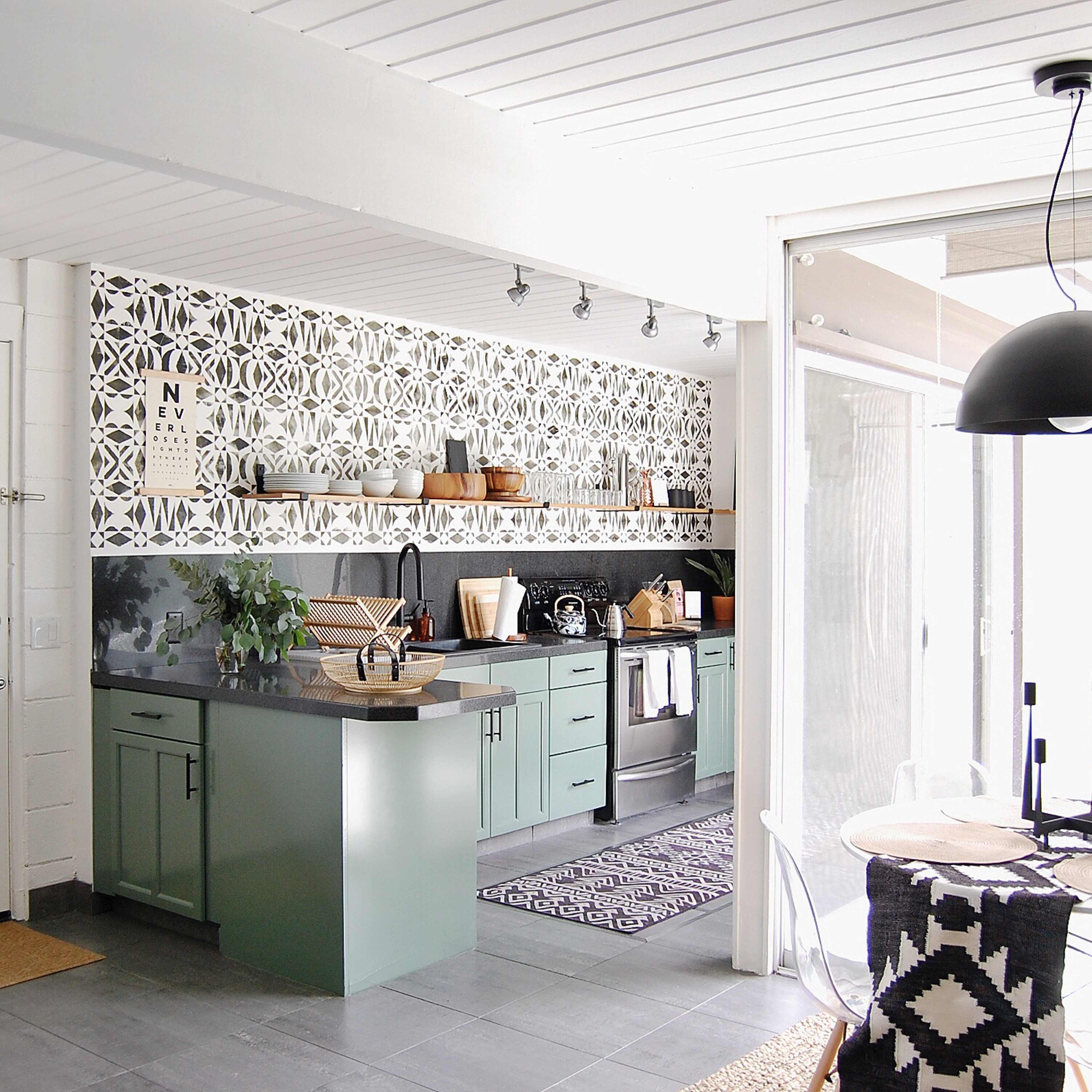 A modern kitchen with green cabinets, a patterned backsplash, and a dining area featuring a round table and wicker chairs.