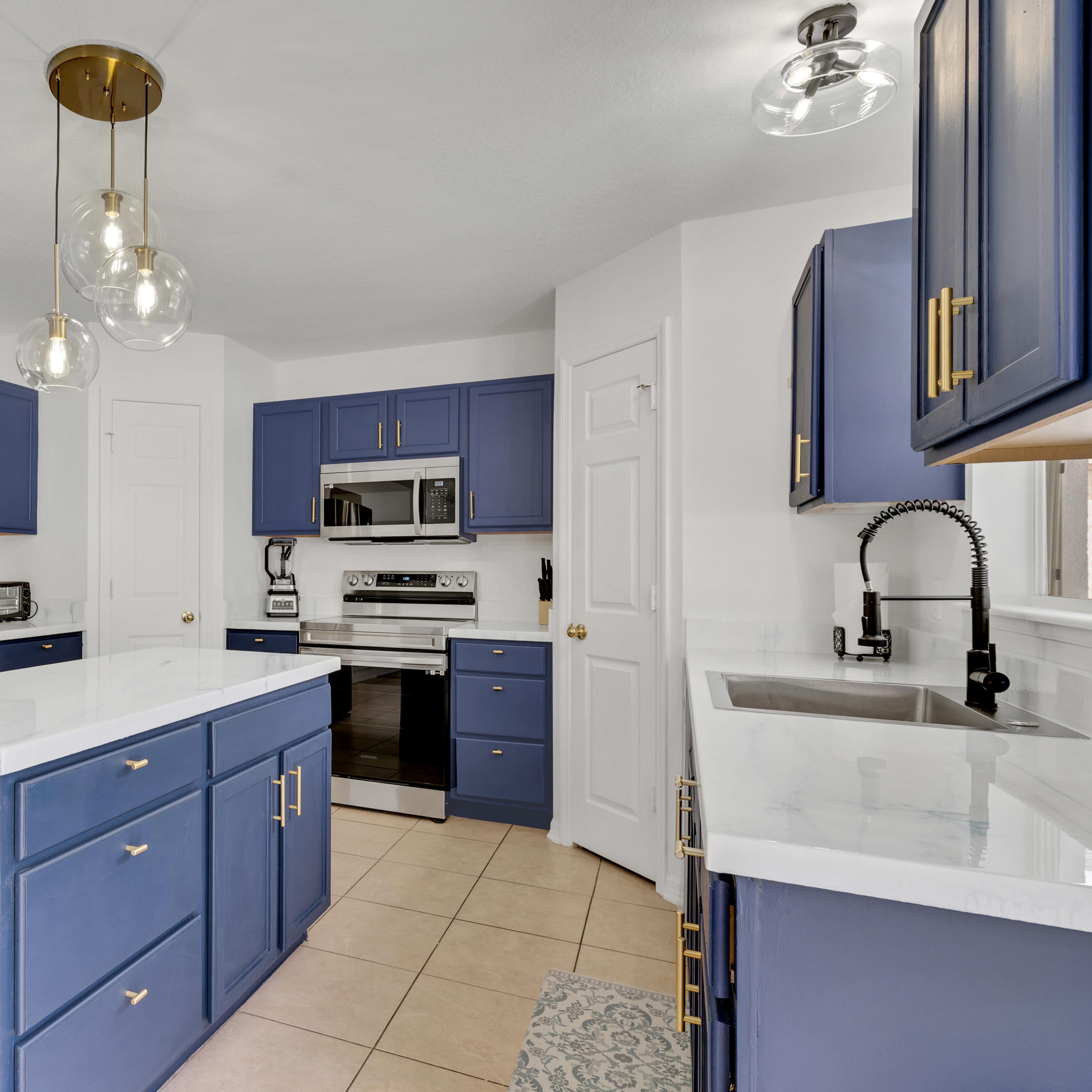 The kitchen features navy blue cabinets, stainless steel appliances, and a white marble countertop on an island.