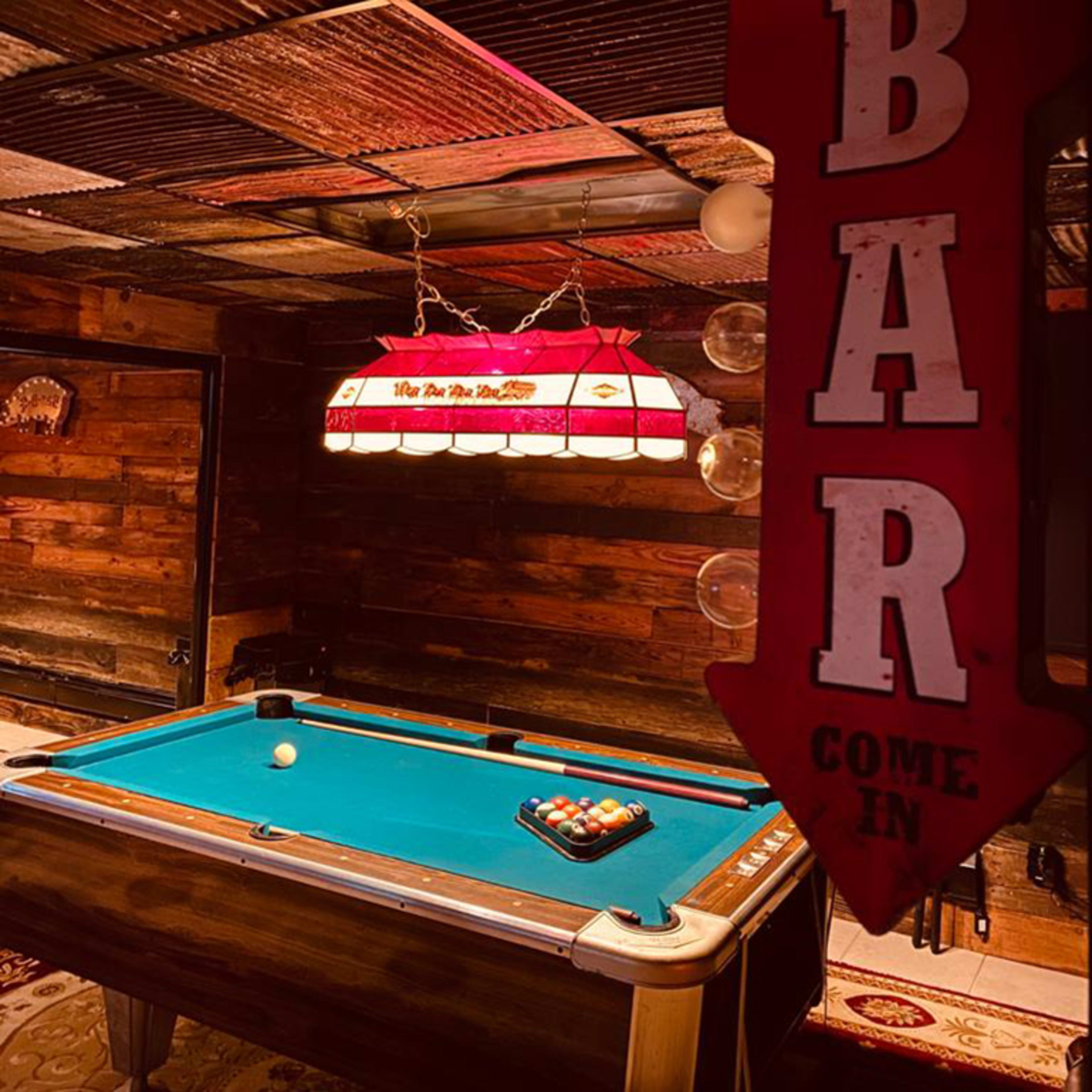 A dimly lit room with a pool table and a prominent sign indicating that the bar is open daily.