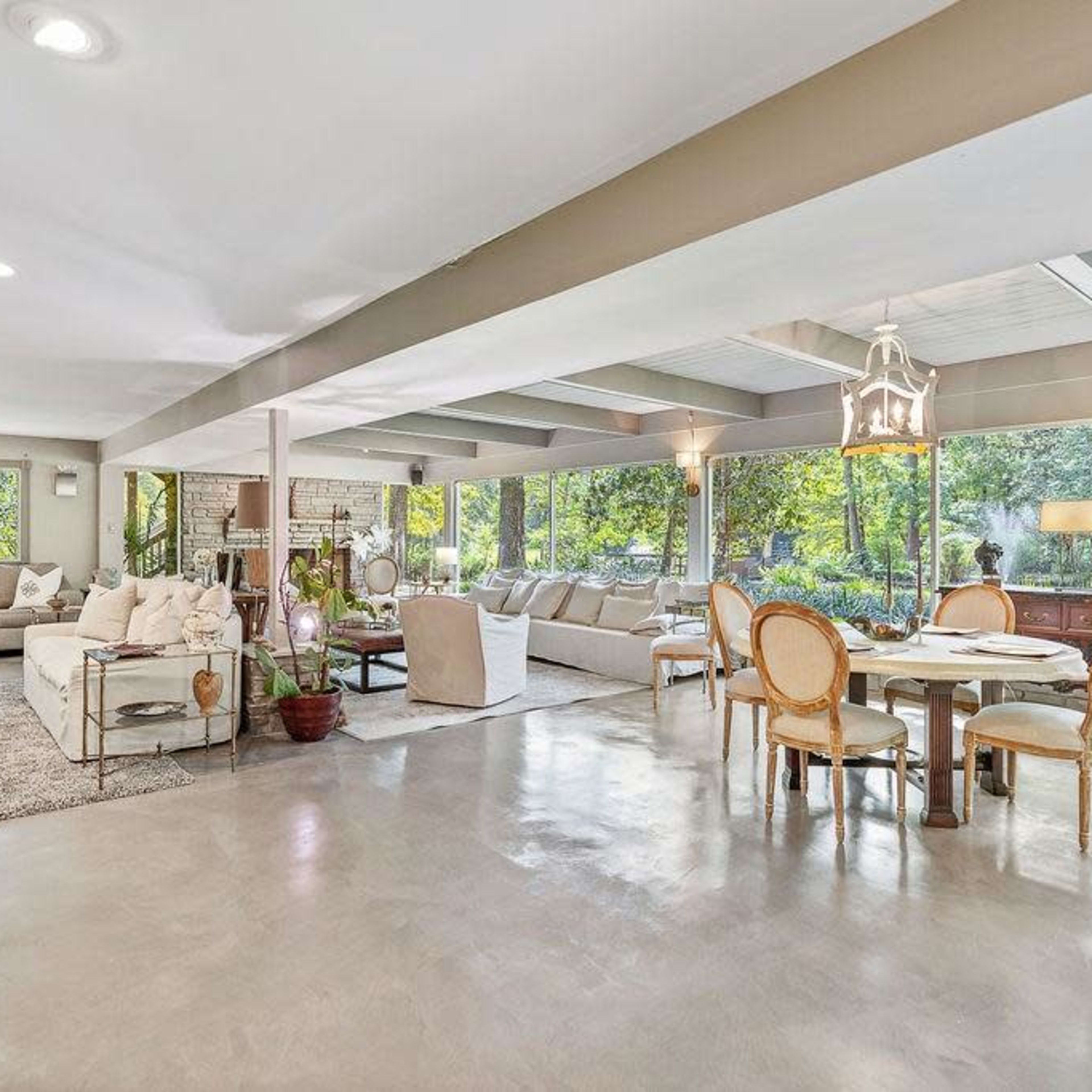 A spacious living area featuring a mix of seating arrangements, a dining table, and large windows overlooking a green landscape.