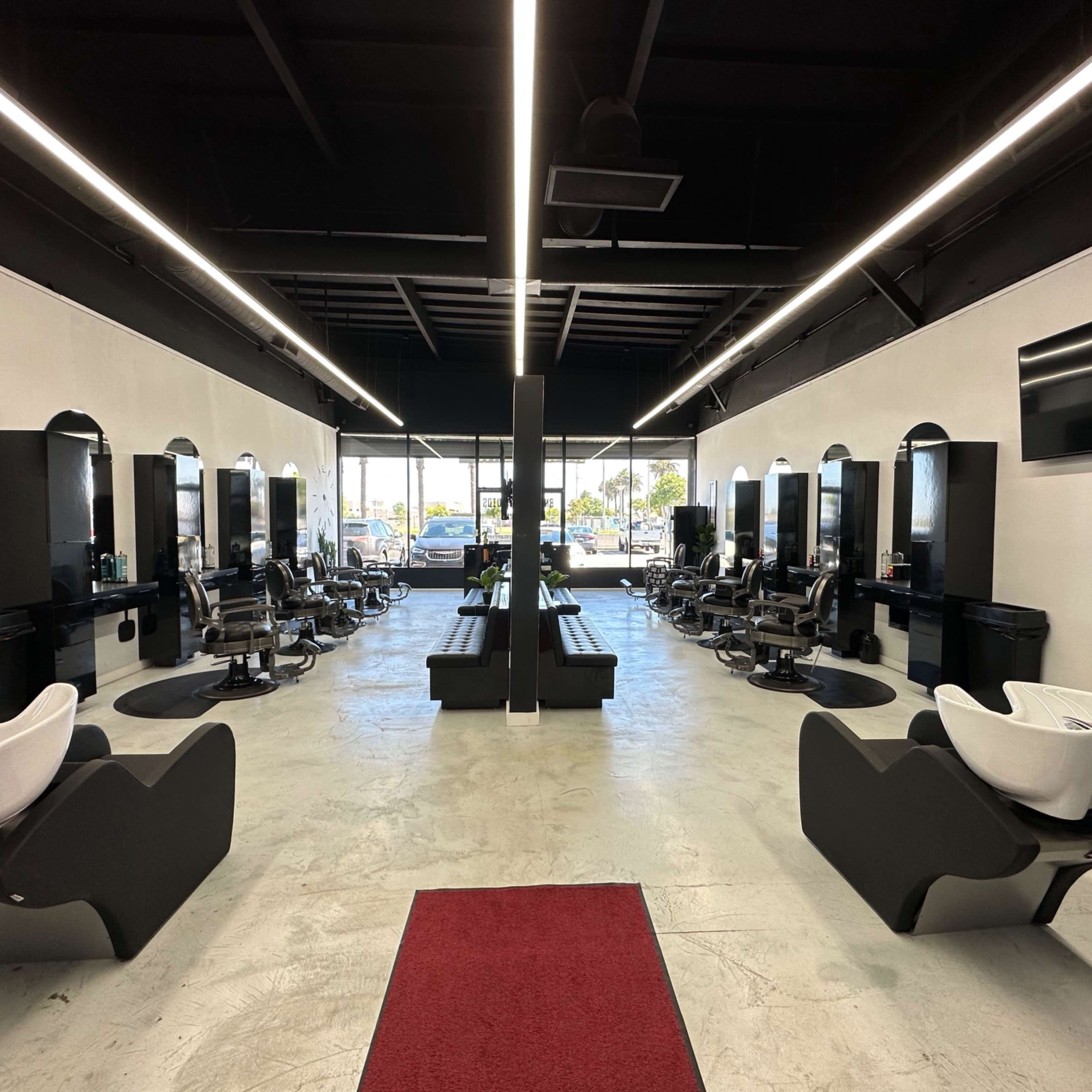 A modern hair salon interior with styling stations on both sides and a central seating area, illuminated by overhead lights.