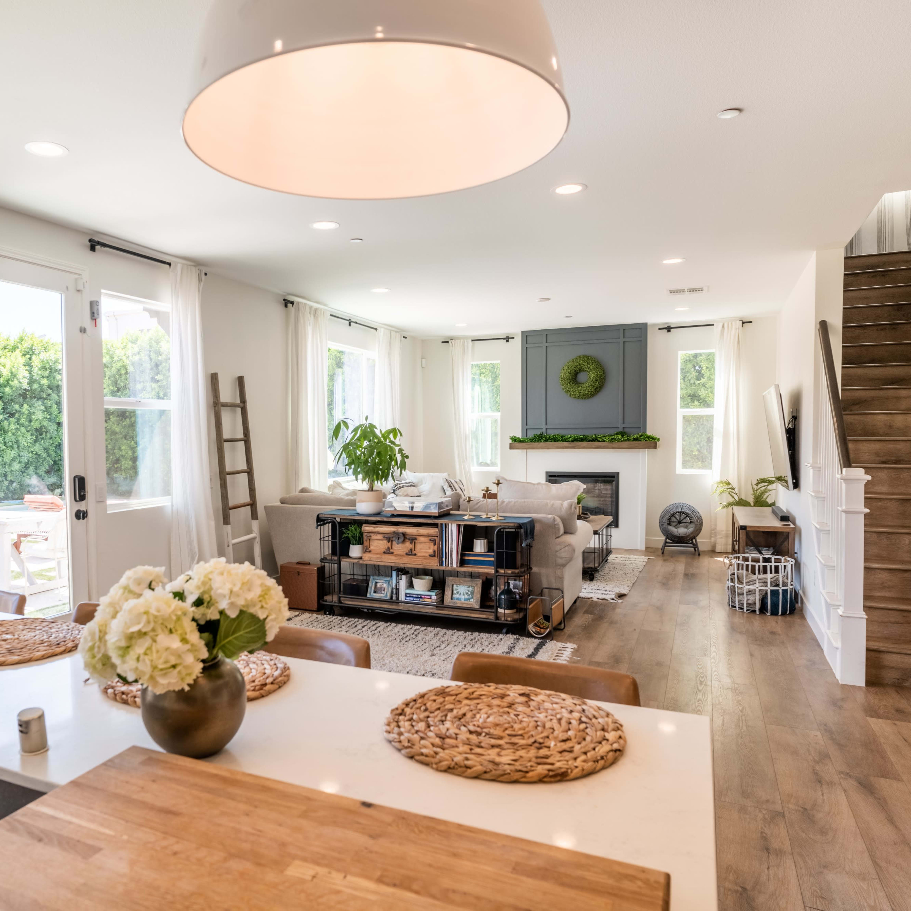 A modern living space features a kitchen island with seating, a cozy seating area with a fireplace, and a staircase leading to an upper level.