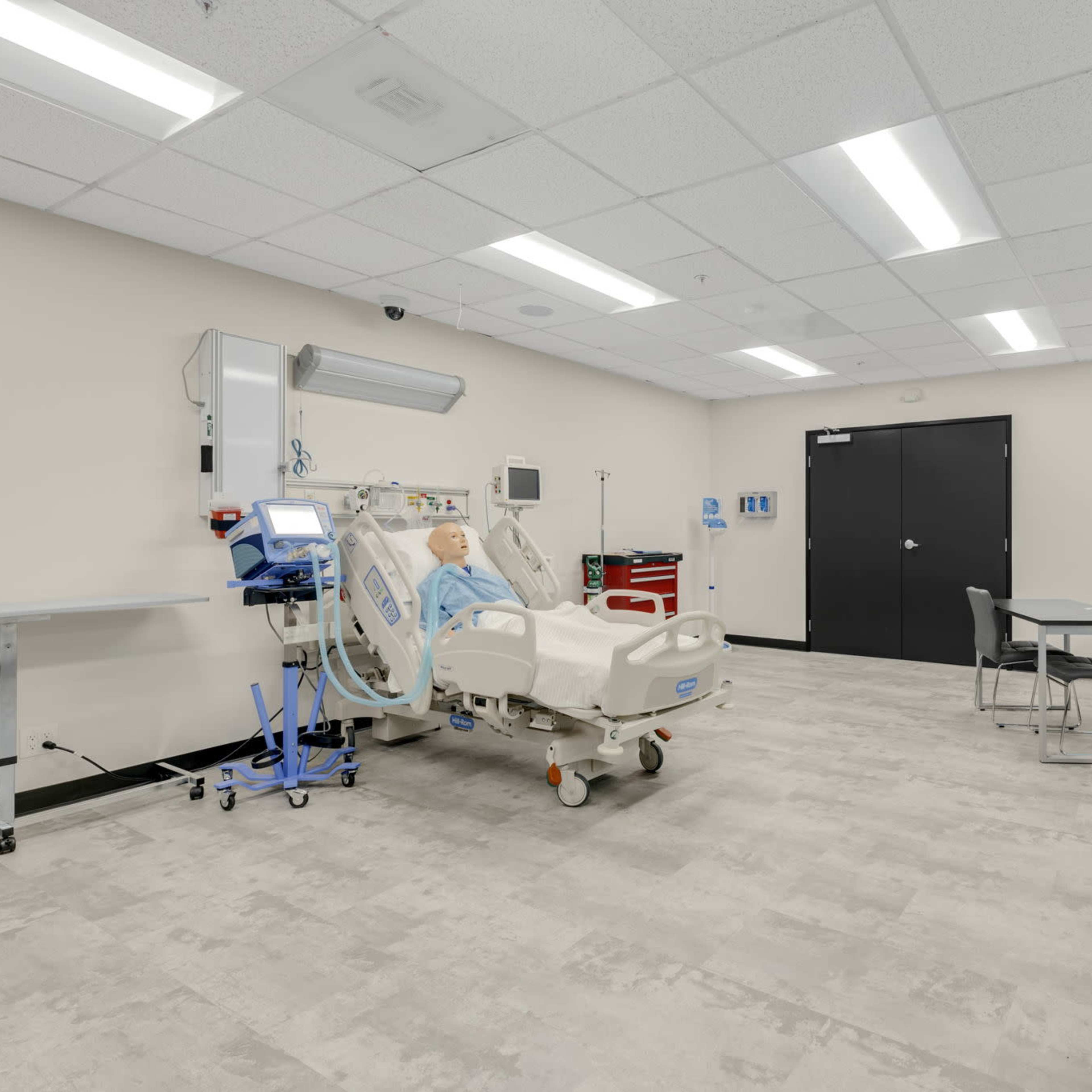 A clean hospital room equipped with a hospital bed, medical equipment, and a table with chairs.
