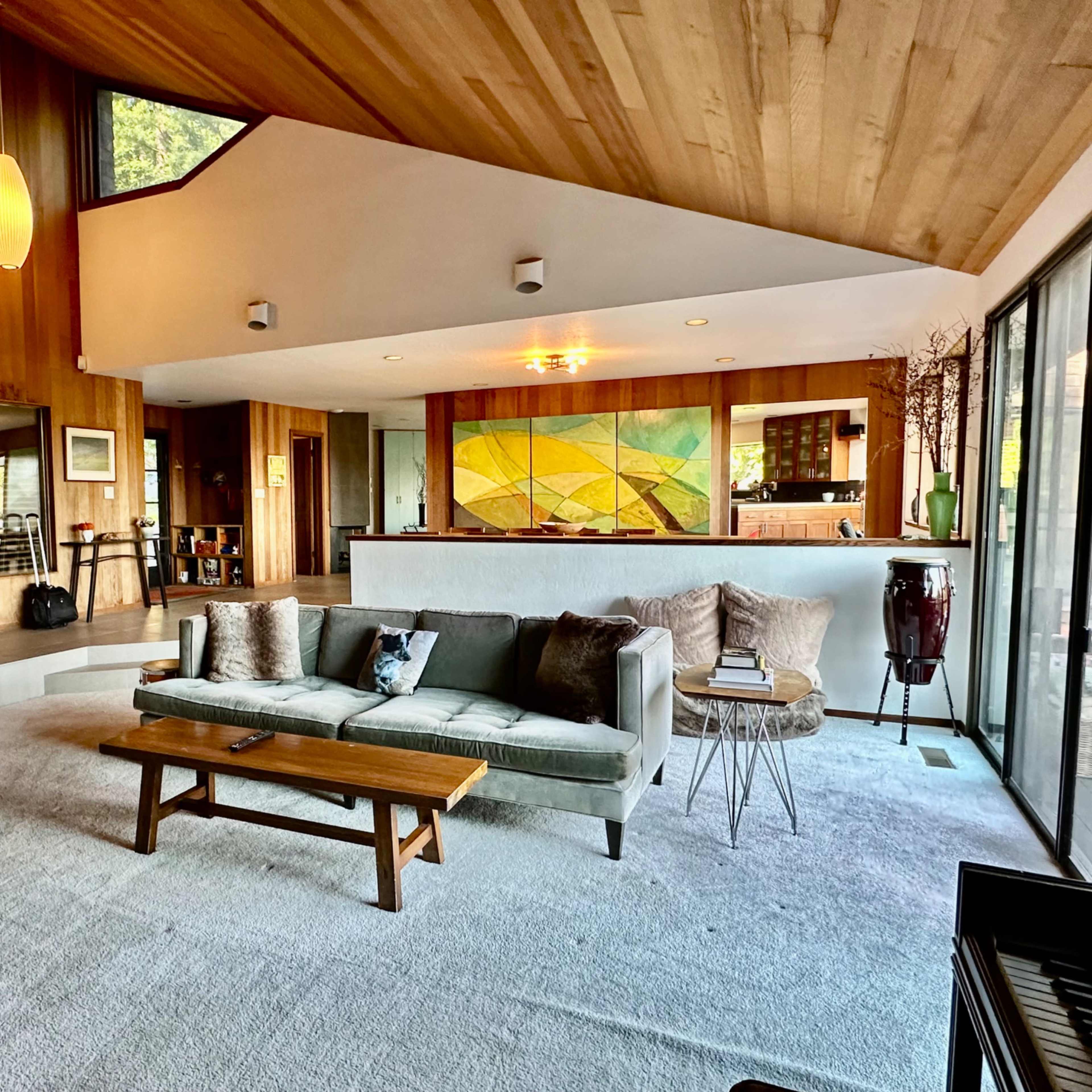 A spacious living room with wooden walls, a large window, a gray sofa, and a coffee table, featuring a modern decorative style.